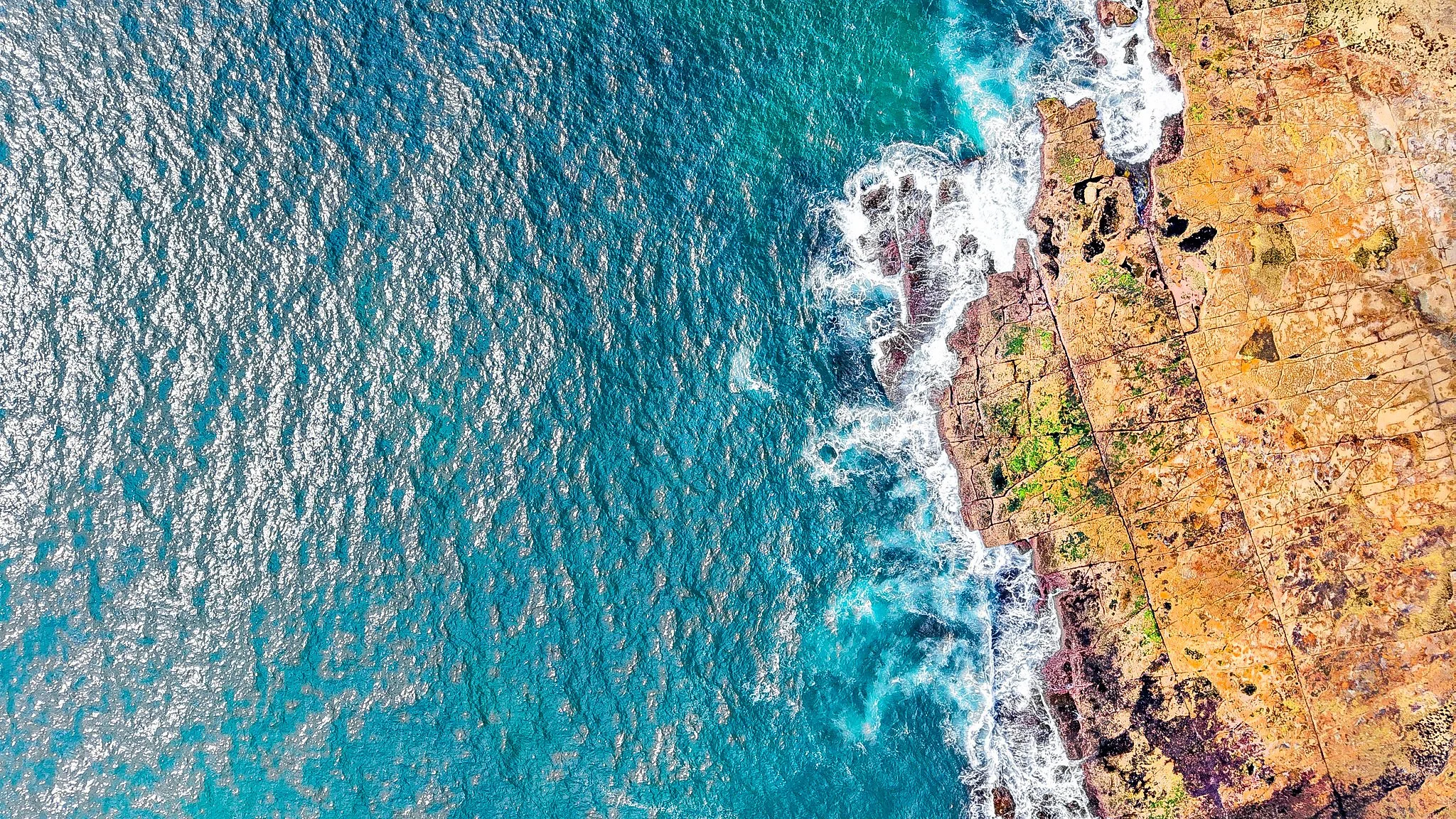 An aerial view of a rocky coastline with waves crashing onto the shore, overlooking the ocean.