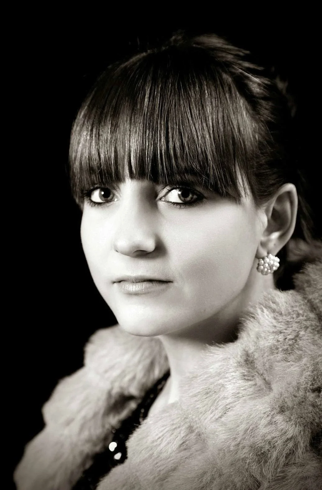Black and white portrait of a woman with short hair and bangs, wearing pearl earrings and a fur coat.
