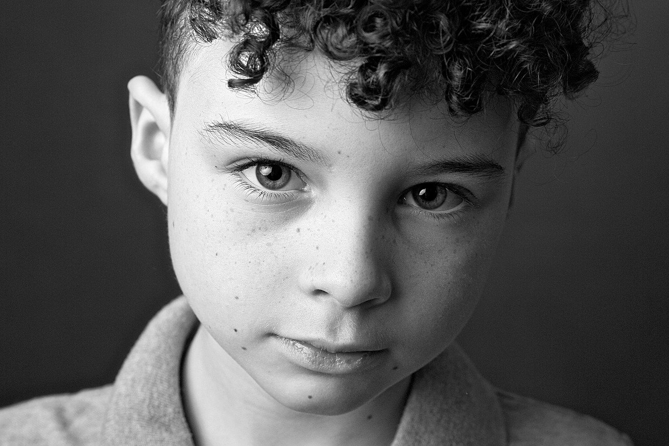 Black and white portrait of a young boy with curly hair, light skin, and freckles, looking directly at the camera.