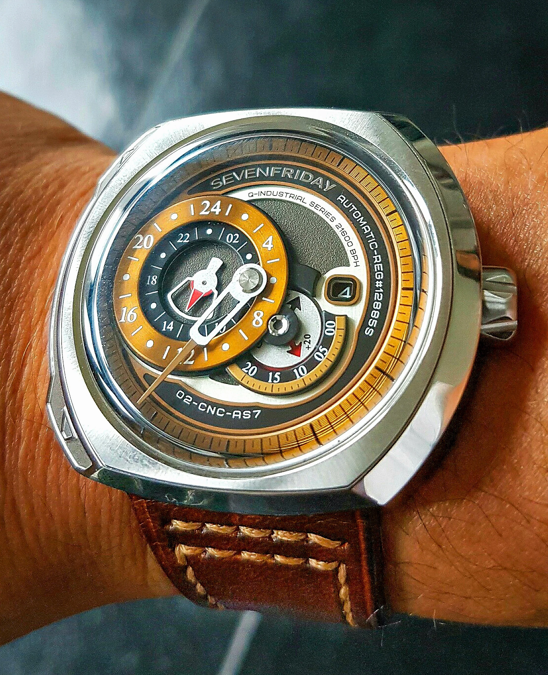 A wristwatch with a black face, orange accents, and multiple subdials, worn on a person's wrist with a brown leather strap.