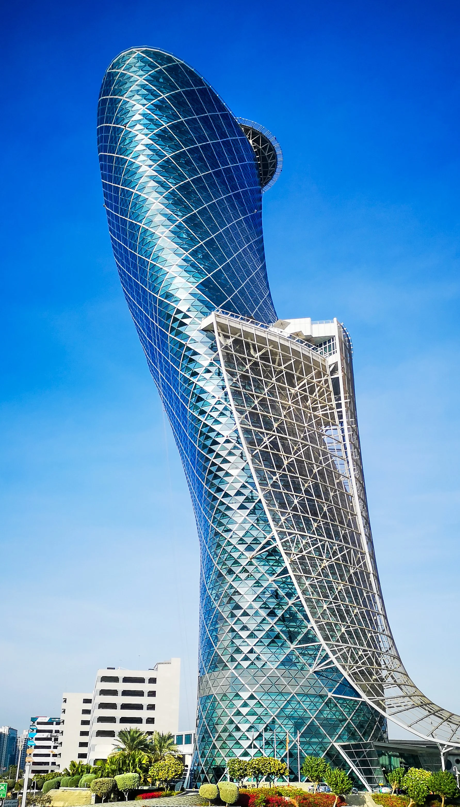 Tall, modern glass skyscraper with a twisting design and a circular observation deck near the top, set against a clear blue sky.