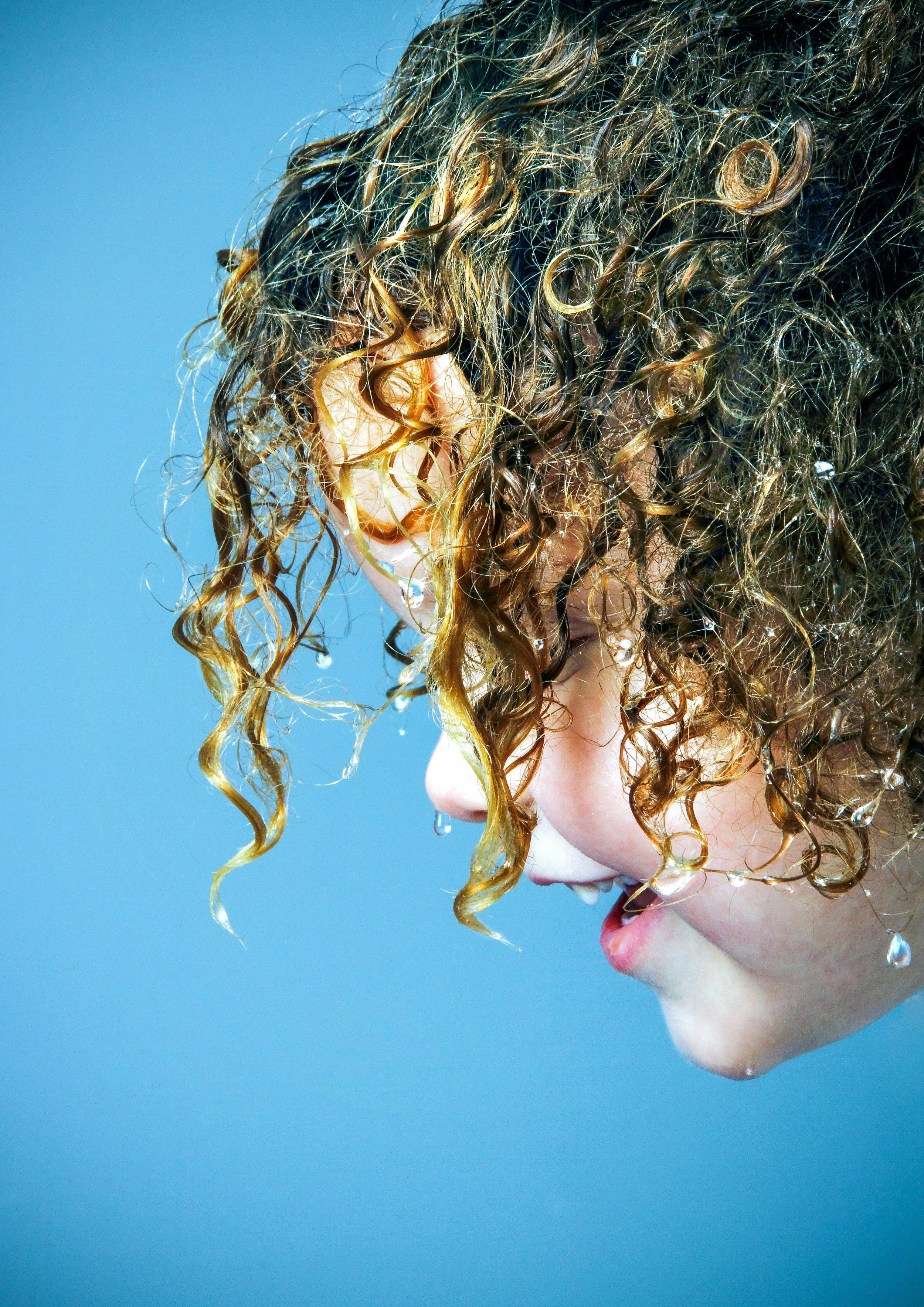 Close-up of a child with curly hair, water droplets on their face, and a blue background.