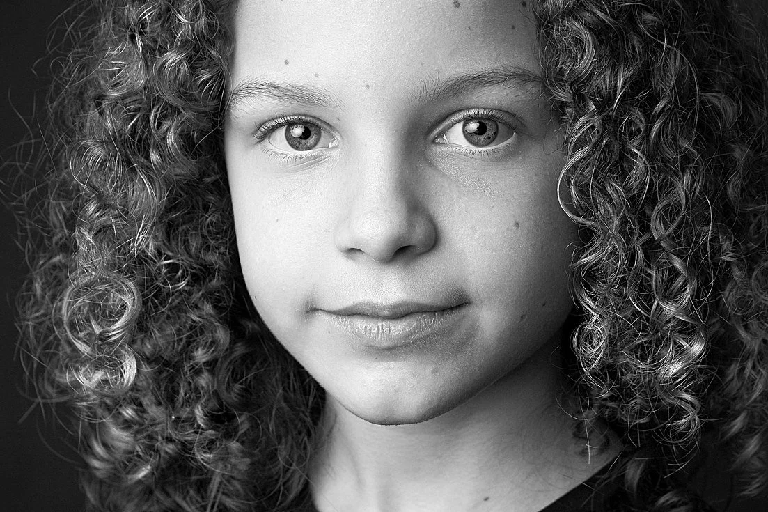 Close-up black and white portrait of a young girl with curly hair and light-colored eyes.
