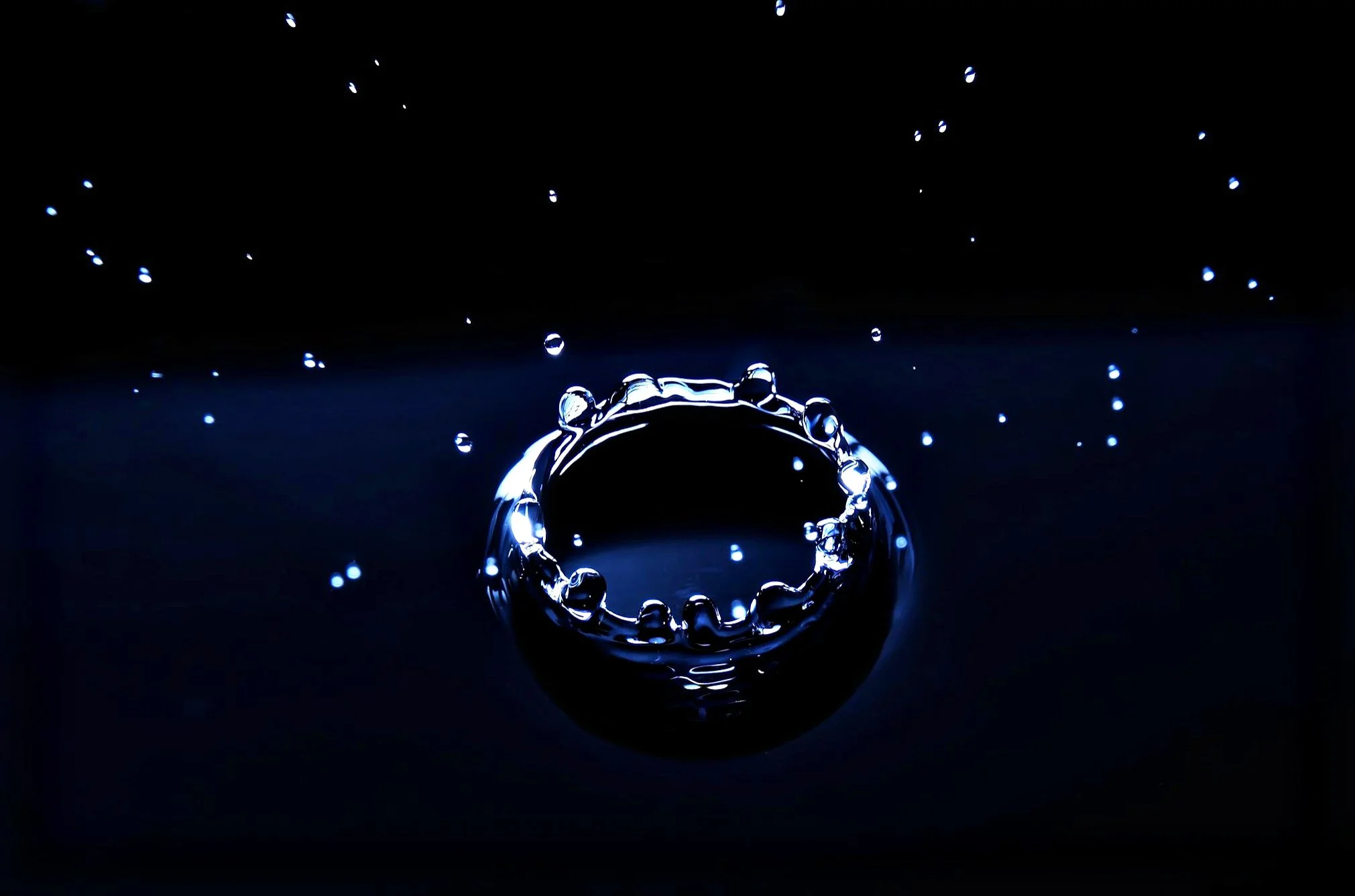 Close-up of a water droplet splash creating a crown-shaped formation on a dark surface with smaller droplets surrounding it.