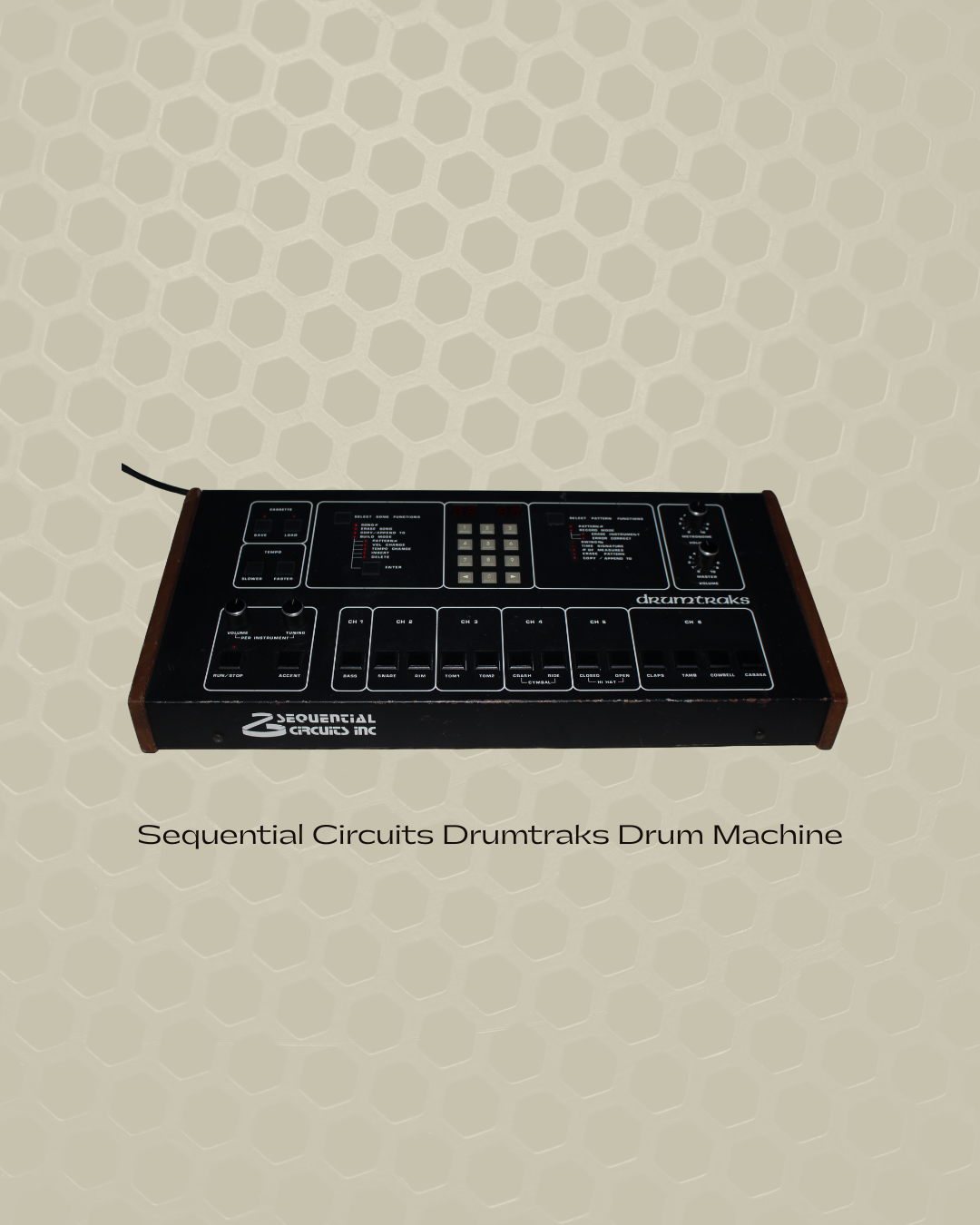 A vintage Sequential Circuits Drumtraks drum machine with black and wooden exterior resting on a honeycomb-patterned surface.