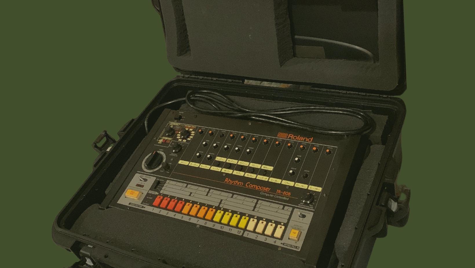 Roland Rhythm Composer TR-808 drum machine inside a black protective case, with various knobs, buttons, and sliders for music production.
