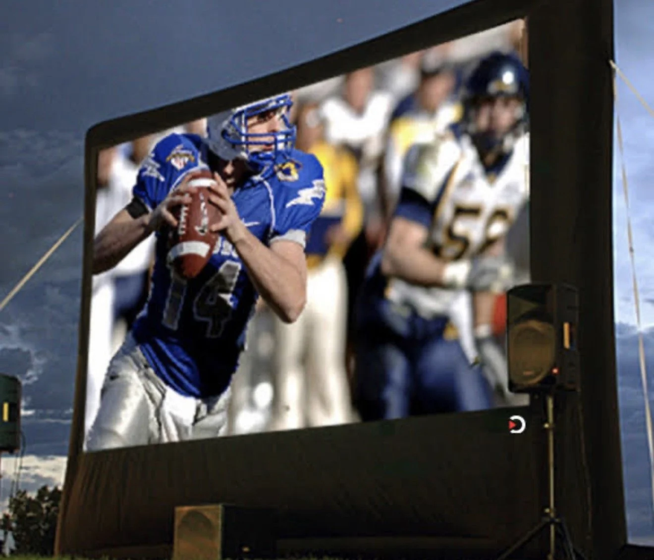 A large outdoor screen displays a football player in a blue jersey holding a football, with other players in the background.