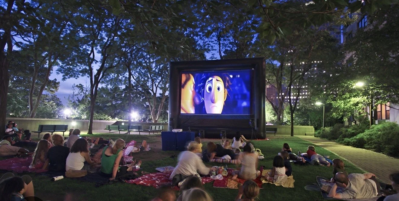 People watching an outdoor movie on a large inflatable screen in a park at dusk.