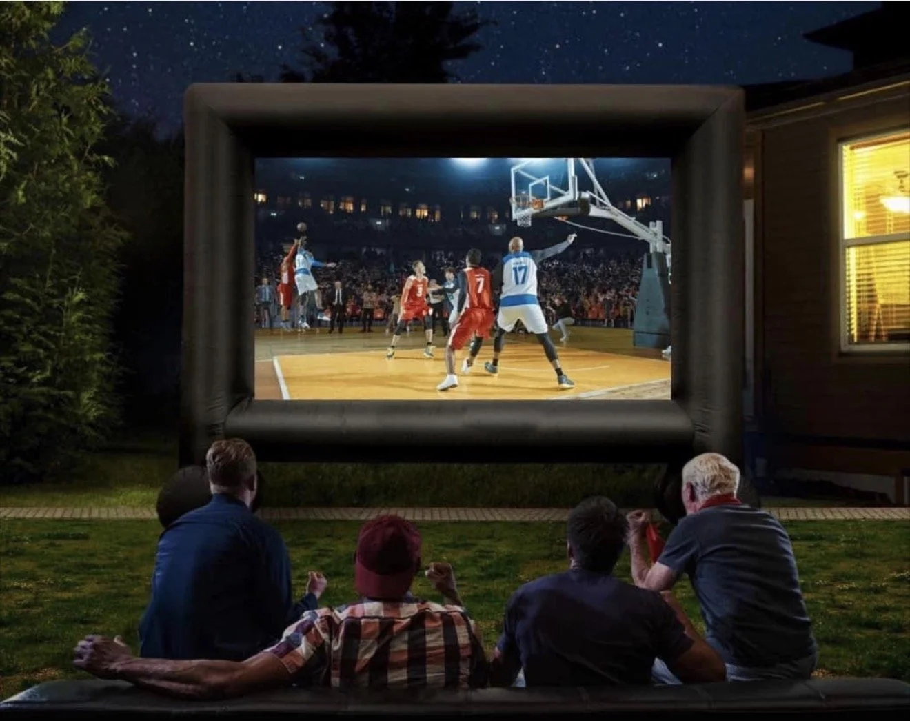 Group of people watching an outdoor movie of a basketball game on a large inflatable screen at night in a backyard.