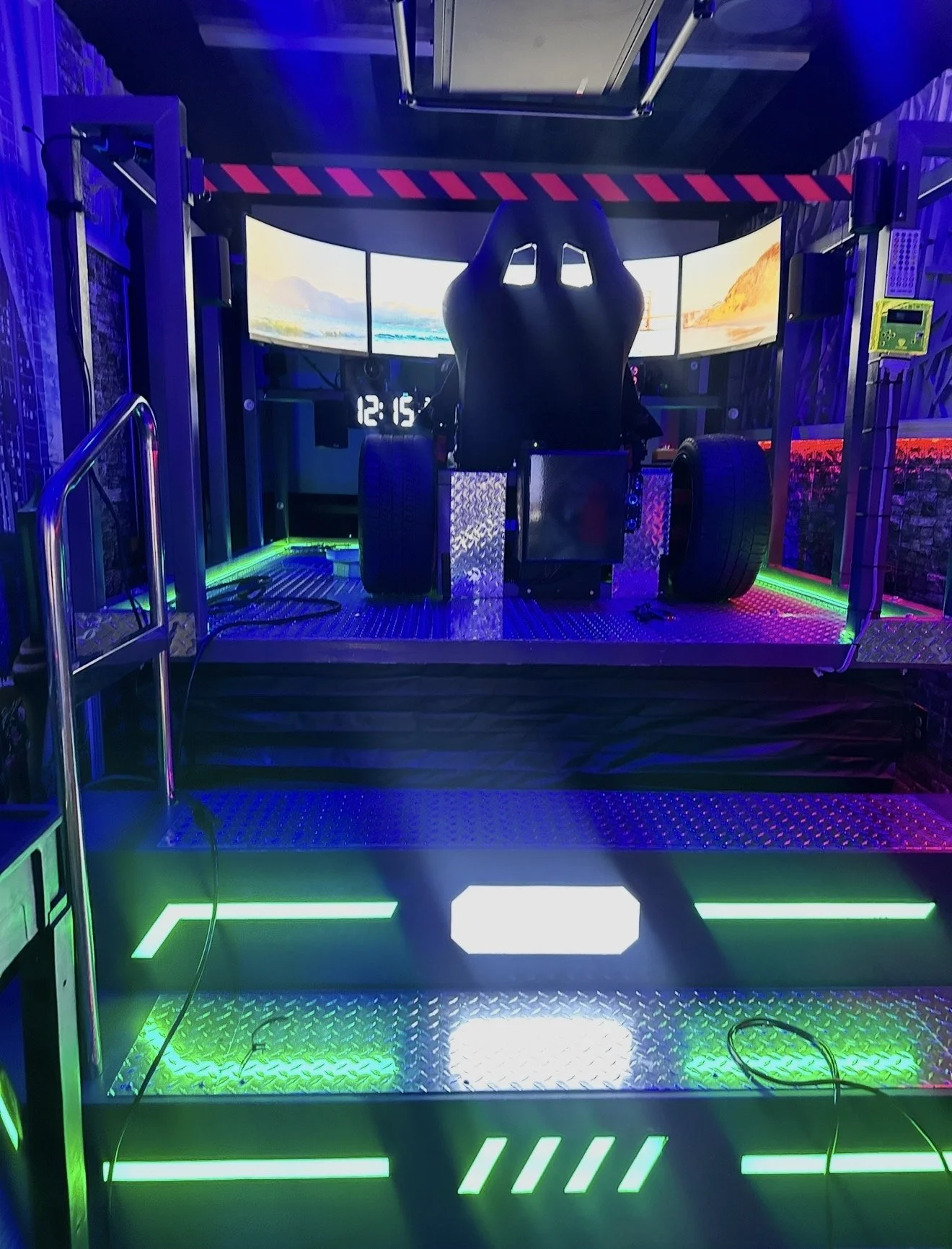 A racing simulator setup with a racing seat, large curved screens, and illuminated green and white LED lights on a metallic platform.