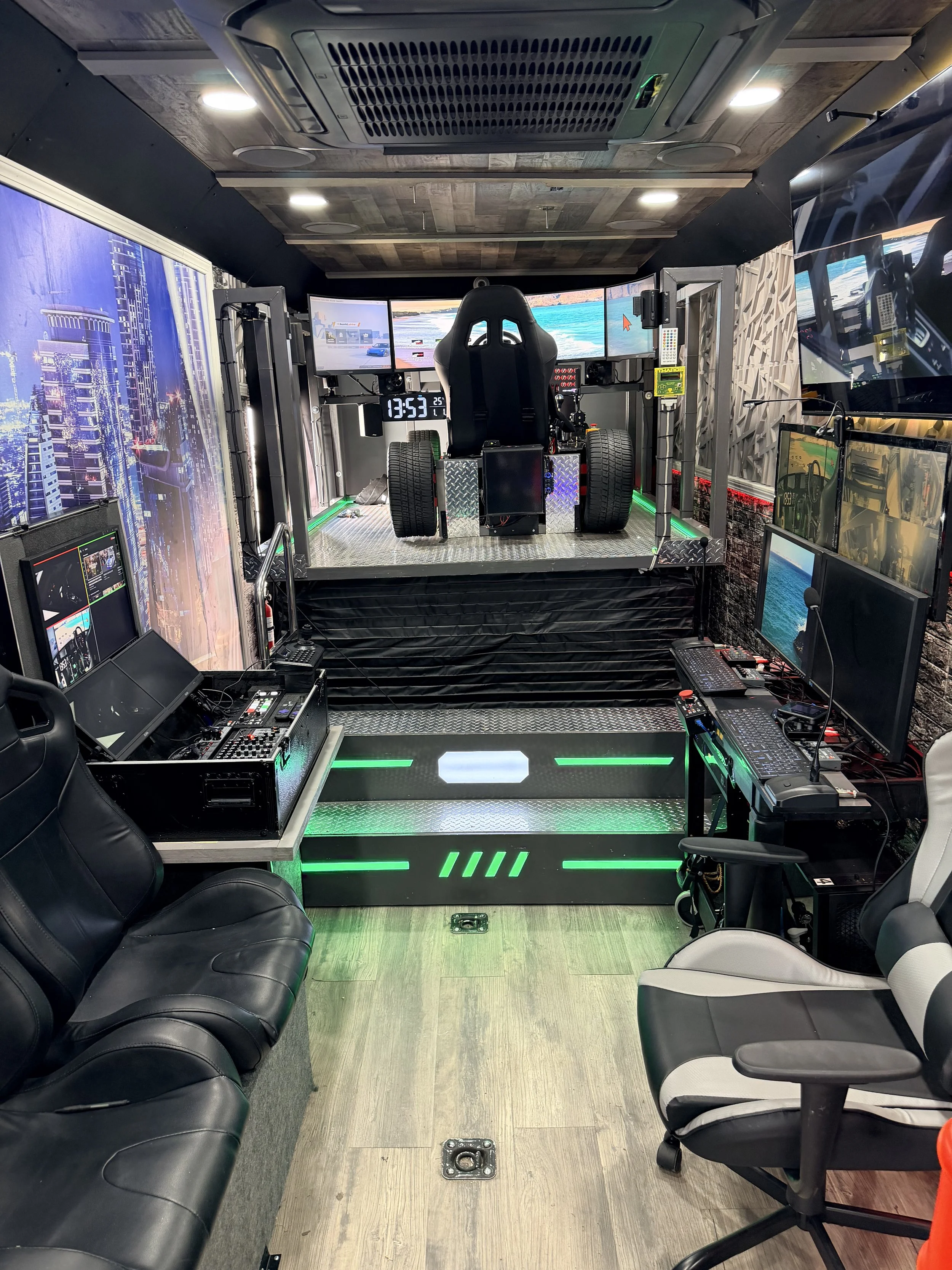 A gaming or simulation setup with multiple monitors displaying a racing game, a racing seat, and various controls. The room has a modern design with cityscape wallpapers, gaming chairs, and LED lighting.