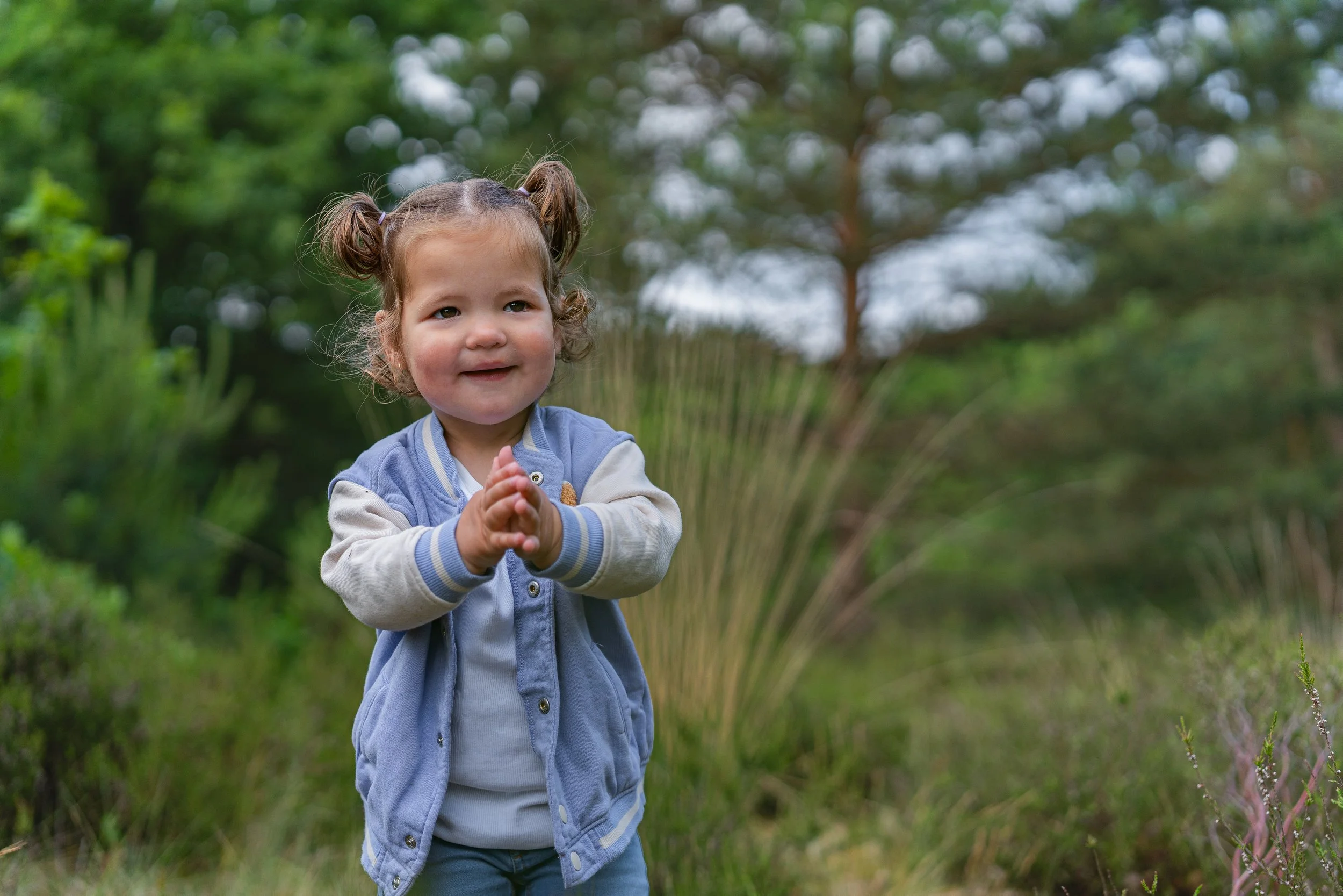 Kleine meisje met twee paardenstaarten die buiten in een groene tuin speelt, glimlachend en haar handen samen gevouwen.