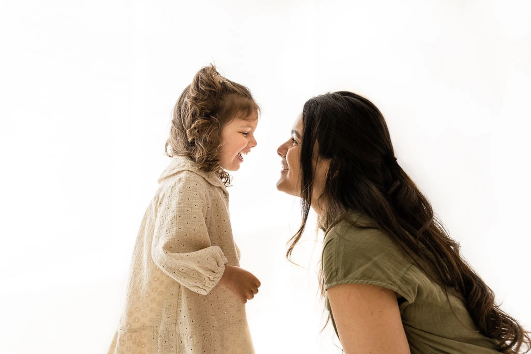 Een jonge vrouw en een meisje die lachend naar elkaar kijken, met een witte achtergrond.