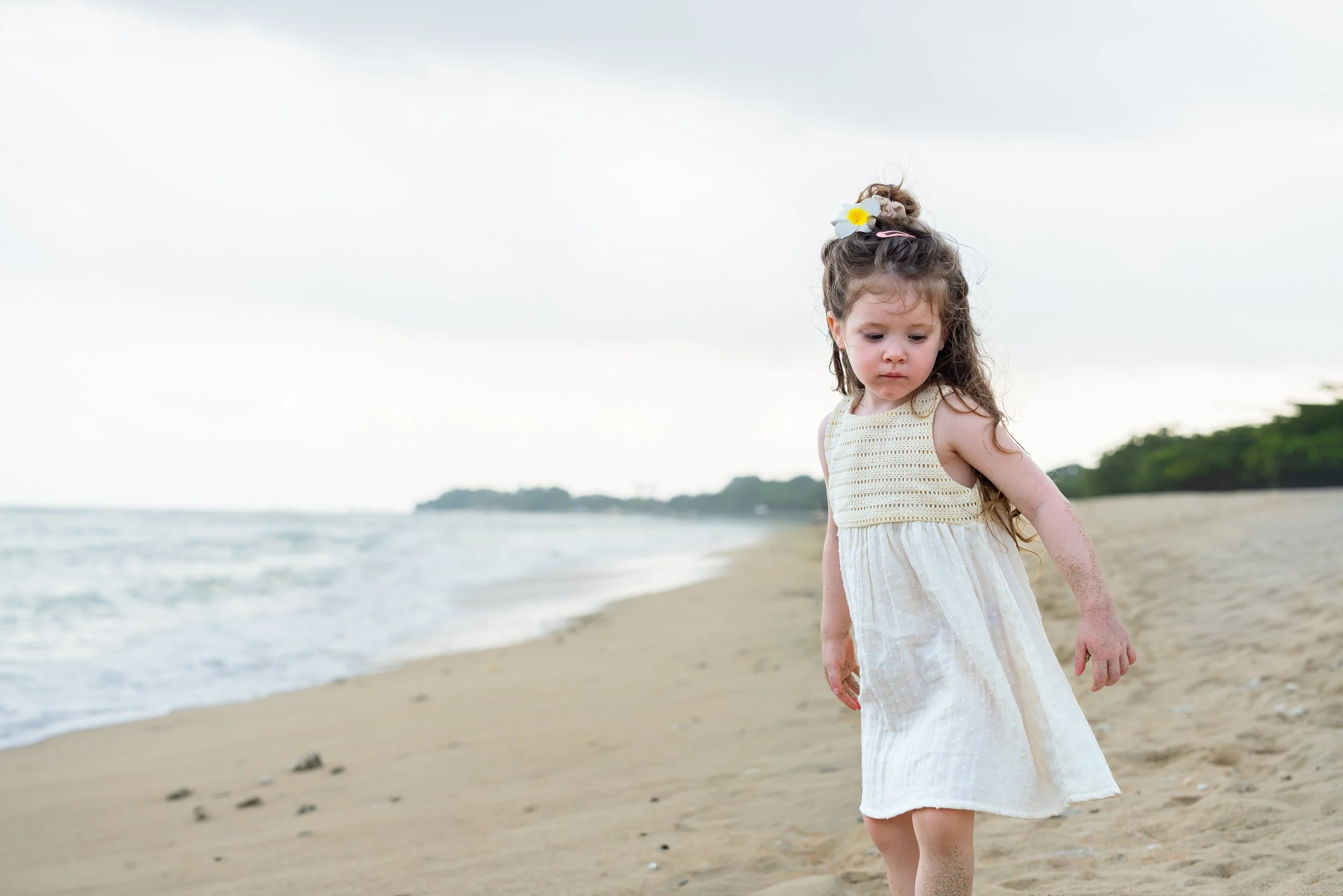 Een jonge meisje met lang haar in een witte jurk loopt op het strand tijdens een bewolkte dag.