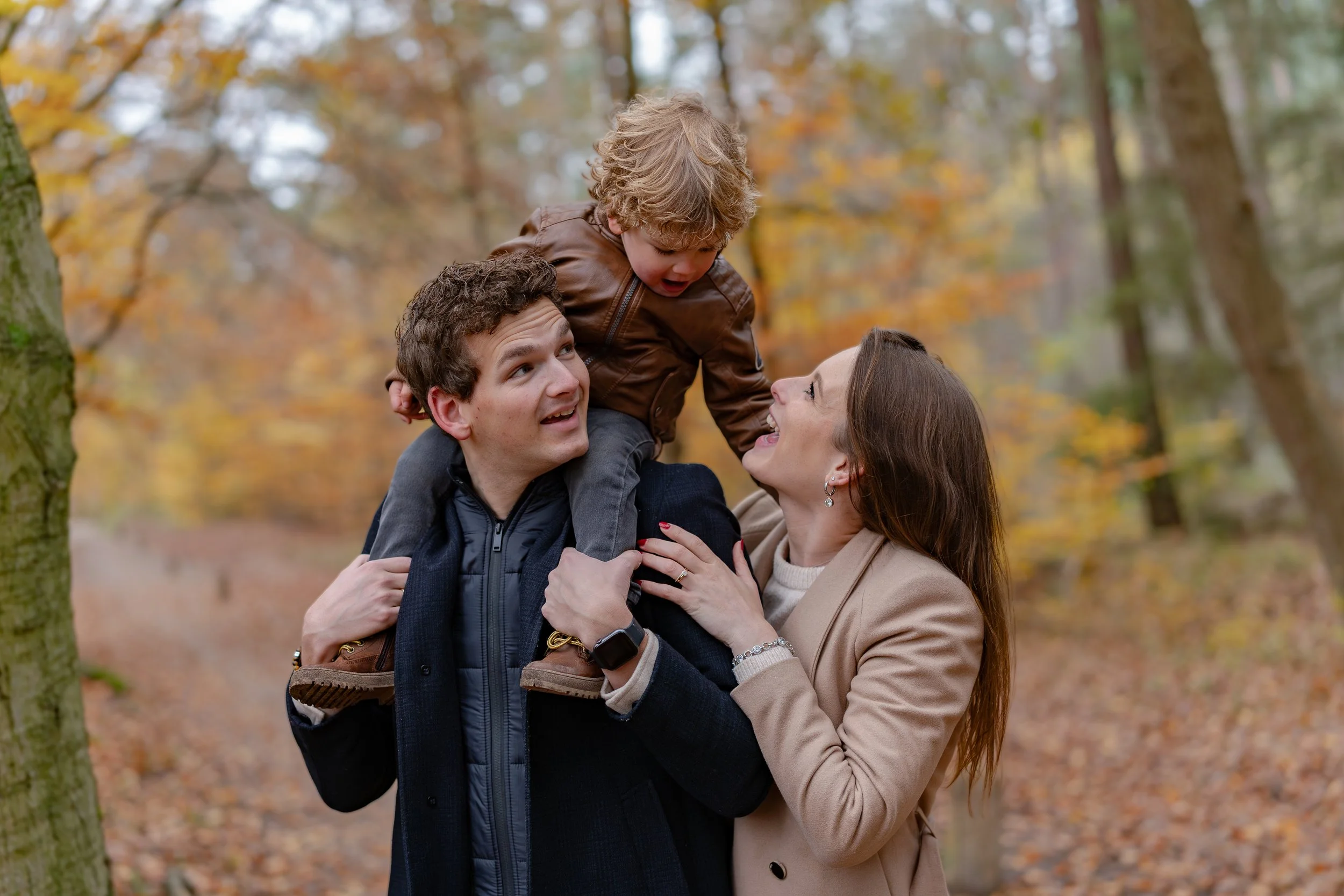 kind opgetild door ouders met bladeren herfst buiten kinderfotografie Noord-Holland