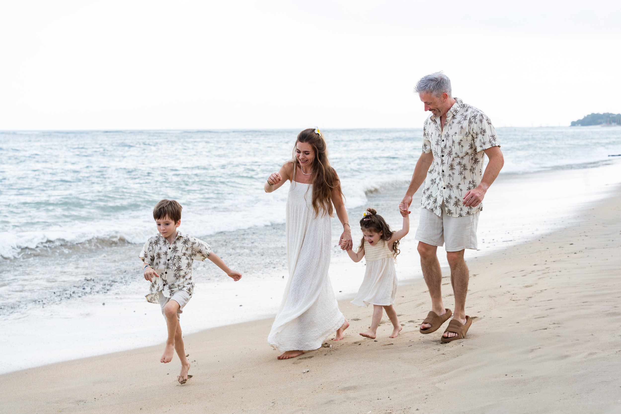 Gezin wandelt hand in hand langs de zee op het strand, lachend en genietend van de dag.