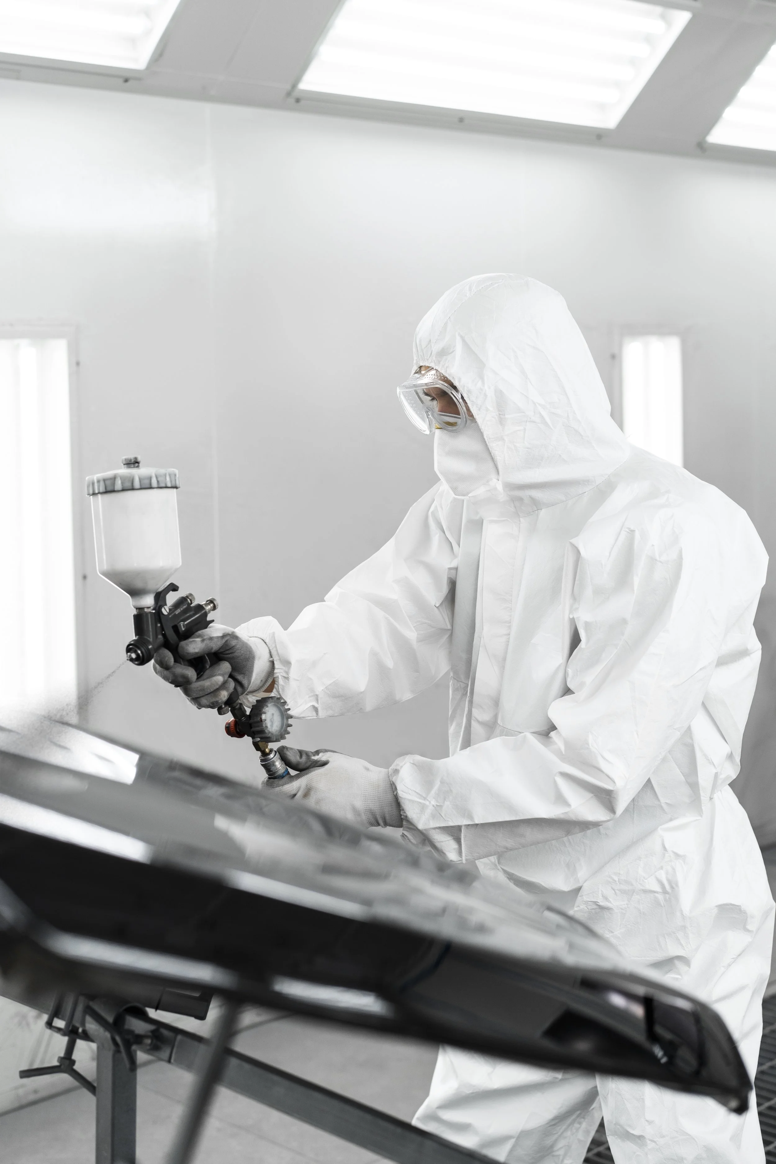 A scientist in protective gear using a spray gun in a laboratory or clean room environment.
