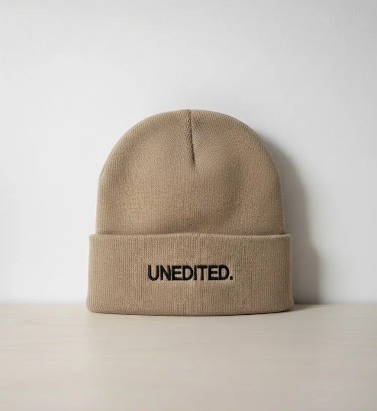 Beige knit beanie hat with the word 'UNEDITED.' embroidered in black on the front.