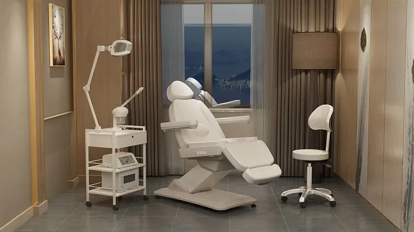 Medical examination room with a dental or gynecological chair, medical equipment on a cart, a white rolling chair, and a window showing a city view at dusk.