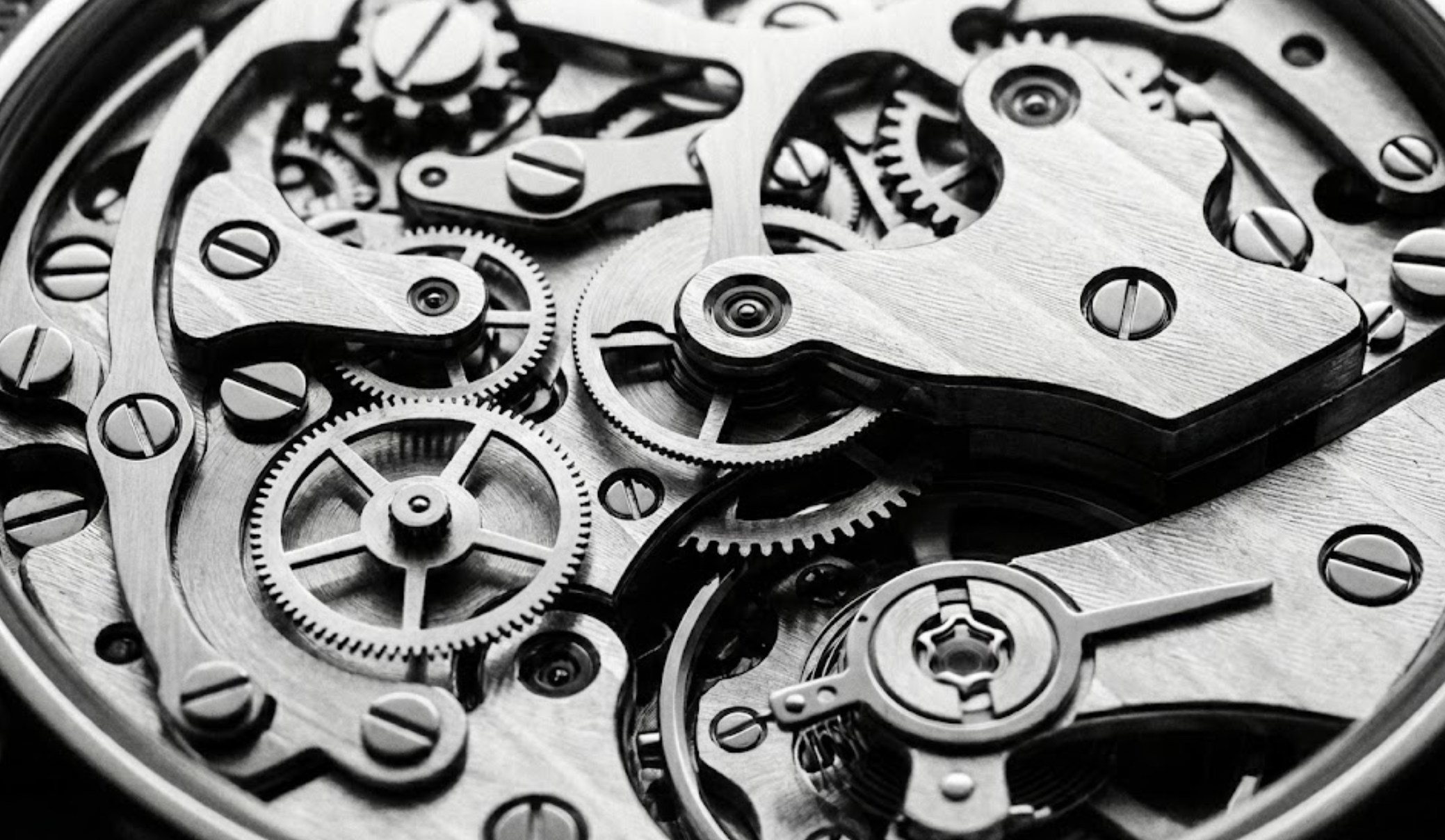 Close-up of a mechanical watch movement showing gears, screws, and intricate components in black and white.