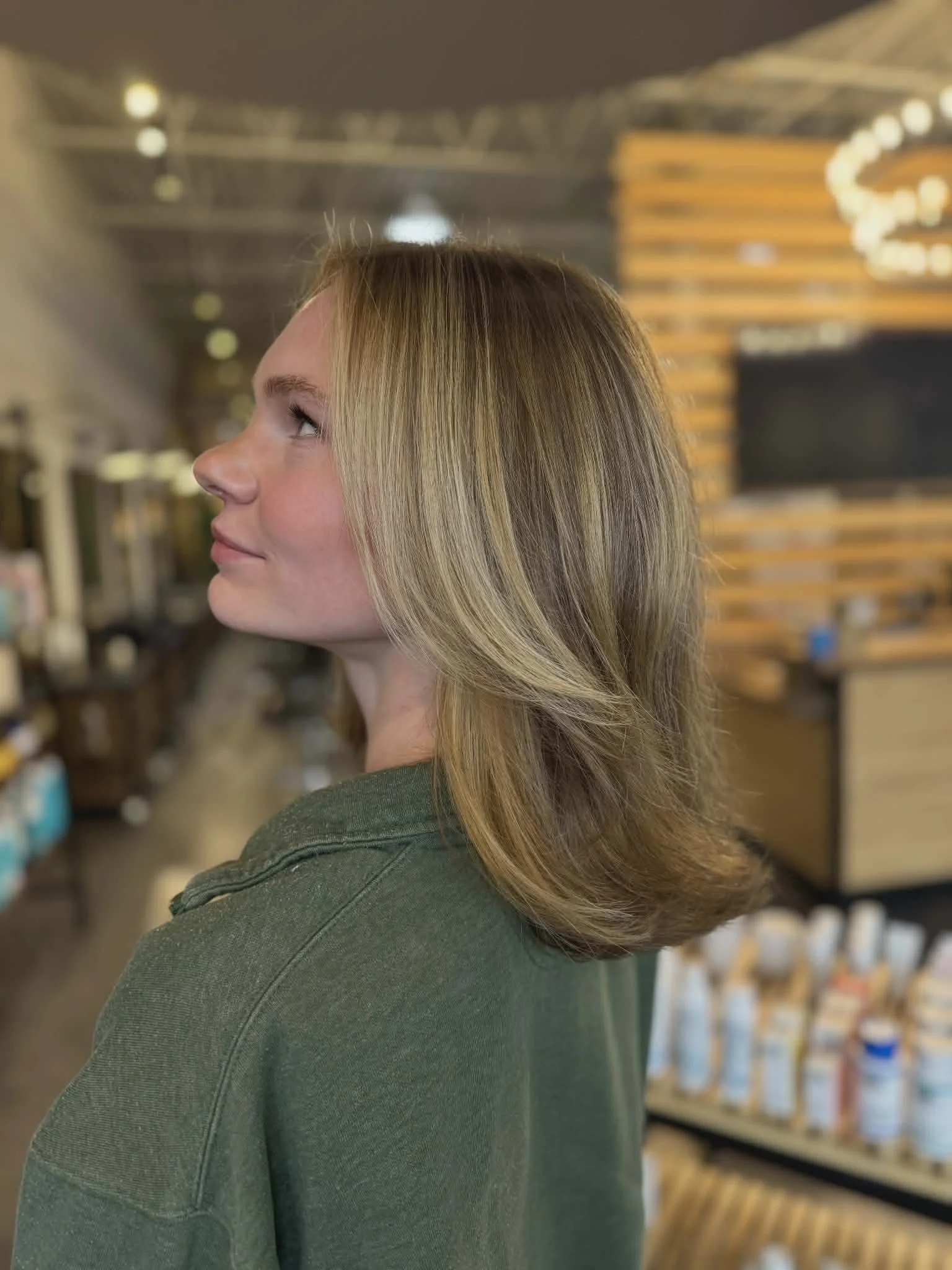 Side view of a blonde woman's head and shoulders in a retail store with hair products in the background.
