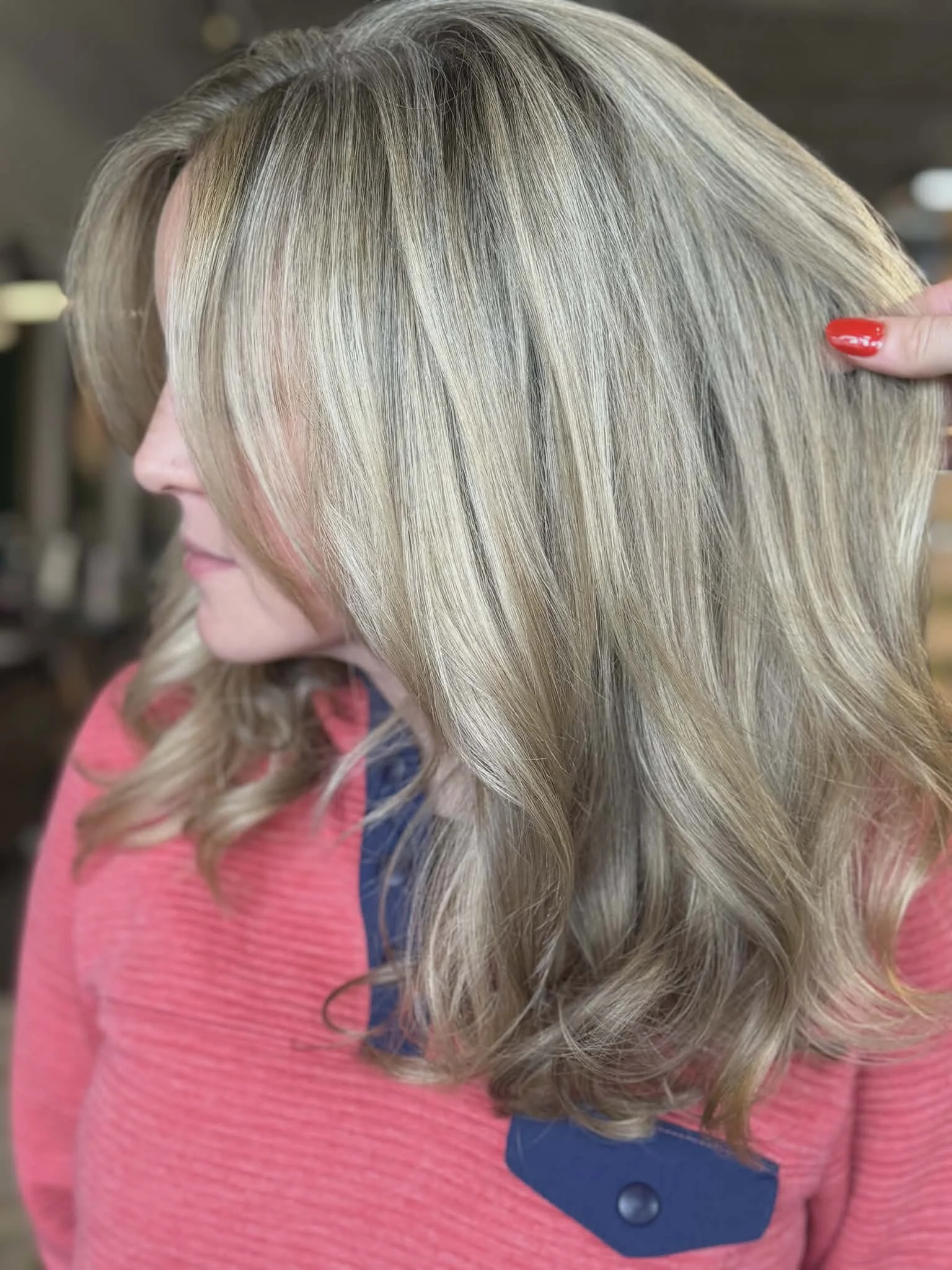 Side view of a woman with shoulder-length blonde hair styled in soft waves, wearing a pink and blue top.