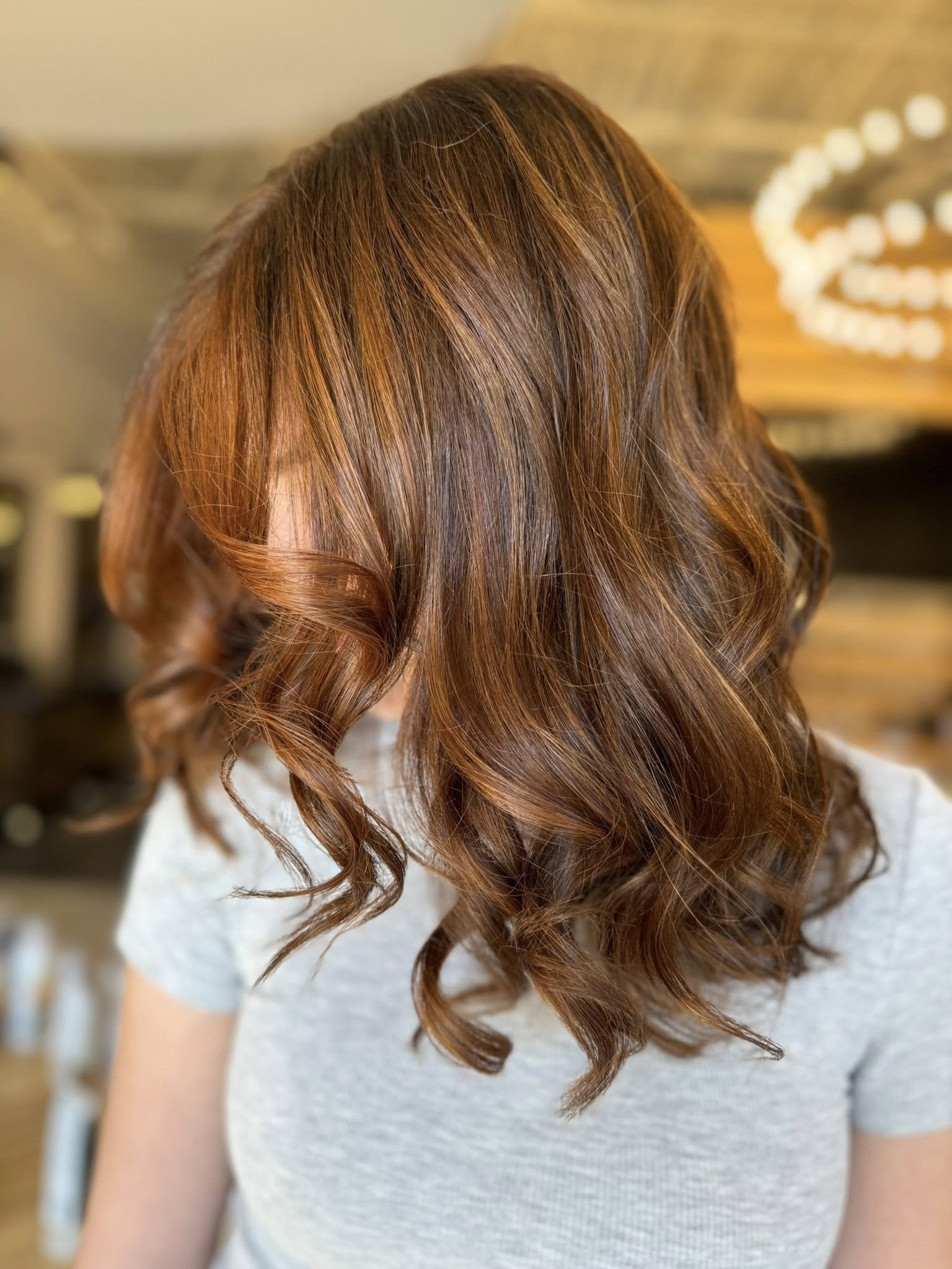 Woman with shoulder-length, wavy, reddish-brown hair viewed from behind.