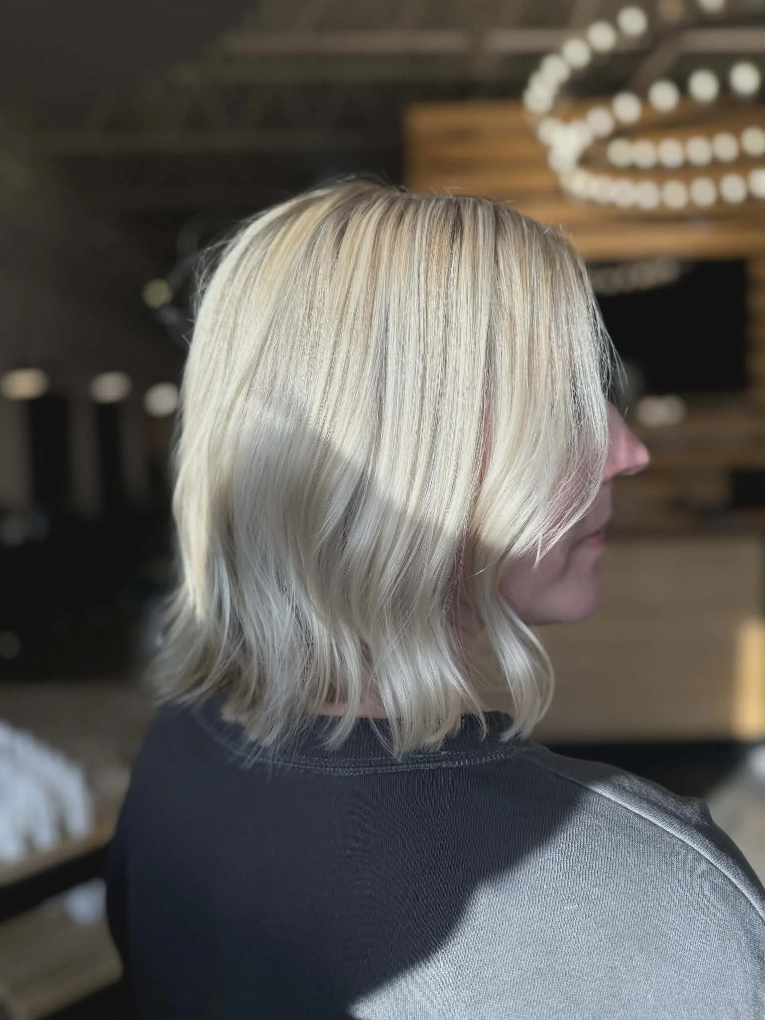 Woman with shoulder-length platinum blonde hair styled in loose waves, wearing a dark shirt.