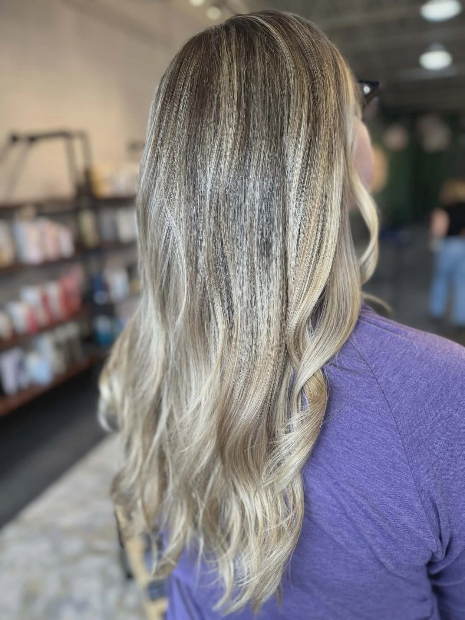 Woman with long blonde, wavy hair in a salon or coffee shop setting.