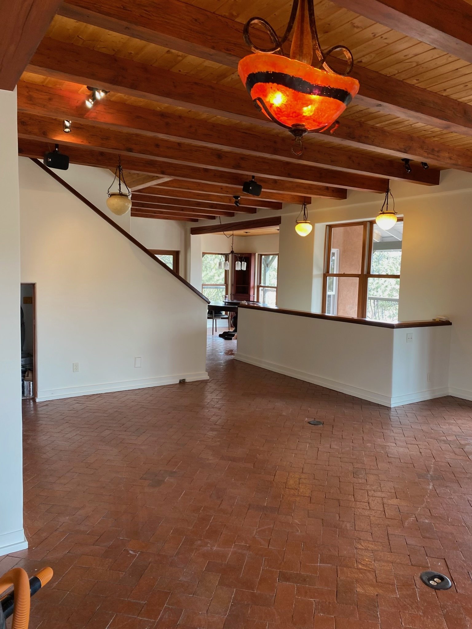 Interior of a house with a wooden beamed ceiling, brick flooring, hanging light fixtures, and large windows.