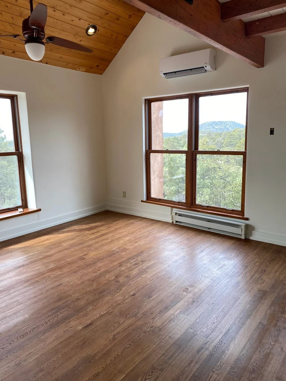 Empty room with hardwood floors, large windows, a ceiling fan, and an air conditioning unit.