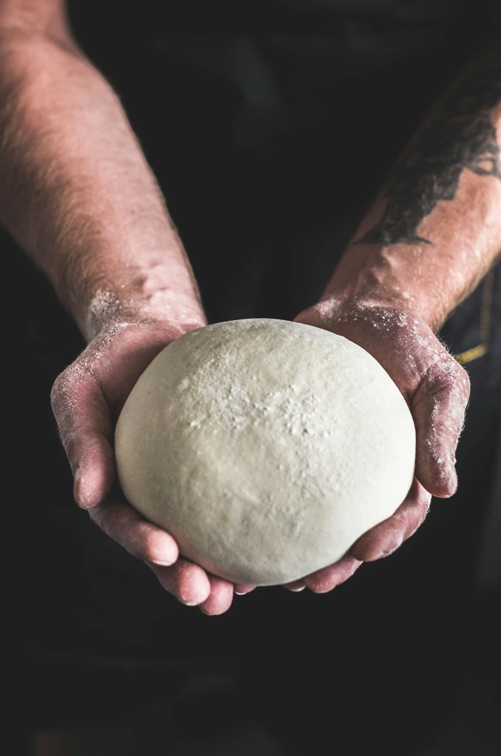 Person holding a round ball of dough with floured hands.