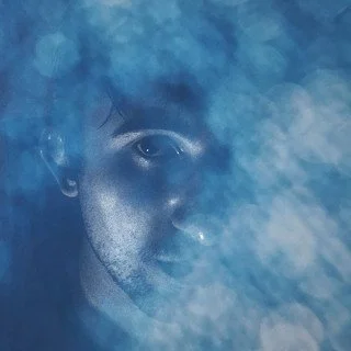 Partial portrait of a person with a serious expression, surrounded by a smoky blue background.