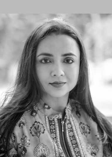 A portrait of a young woman with long dark hair, wearing a patterned traditional top, outdoors with blurred background.