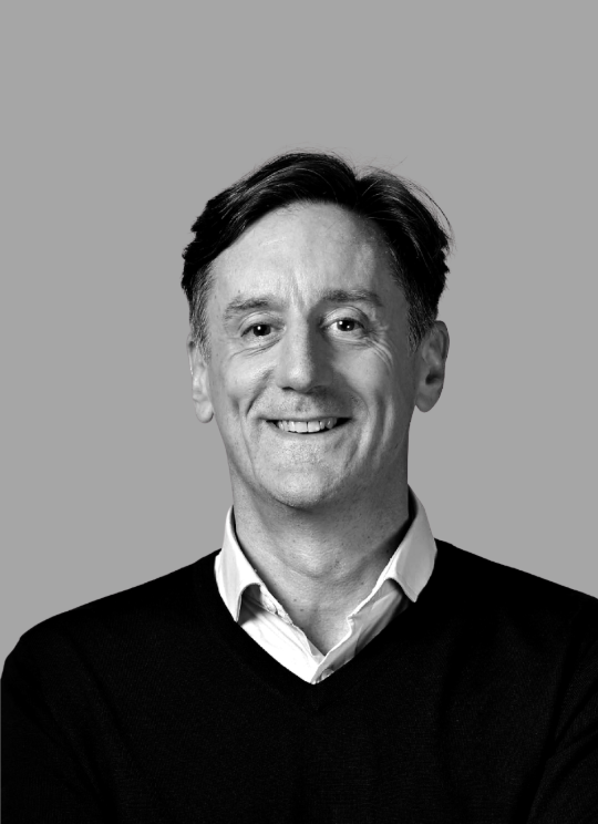 Black and white portrait of a smiling man with dark hair, wearing a collared shirt and sweater, against a plain background.