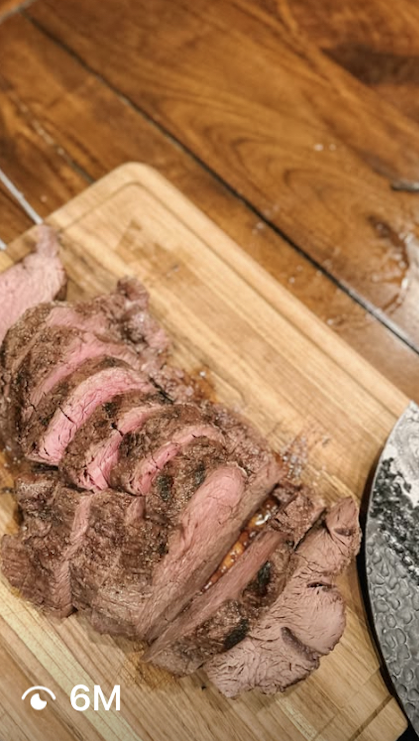 Slices of cooked steak on a wooden cutting board.