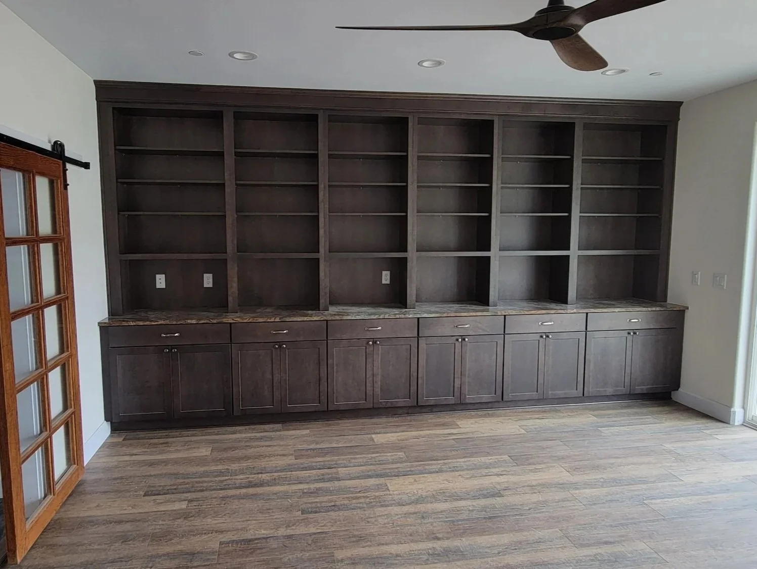 Empty dark wood bookshelf with cabinets and a marble top, located on a hardwood floor, with a ceiling fan above.