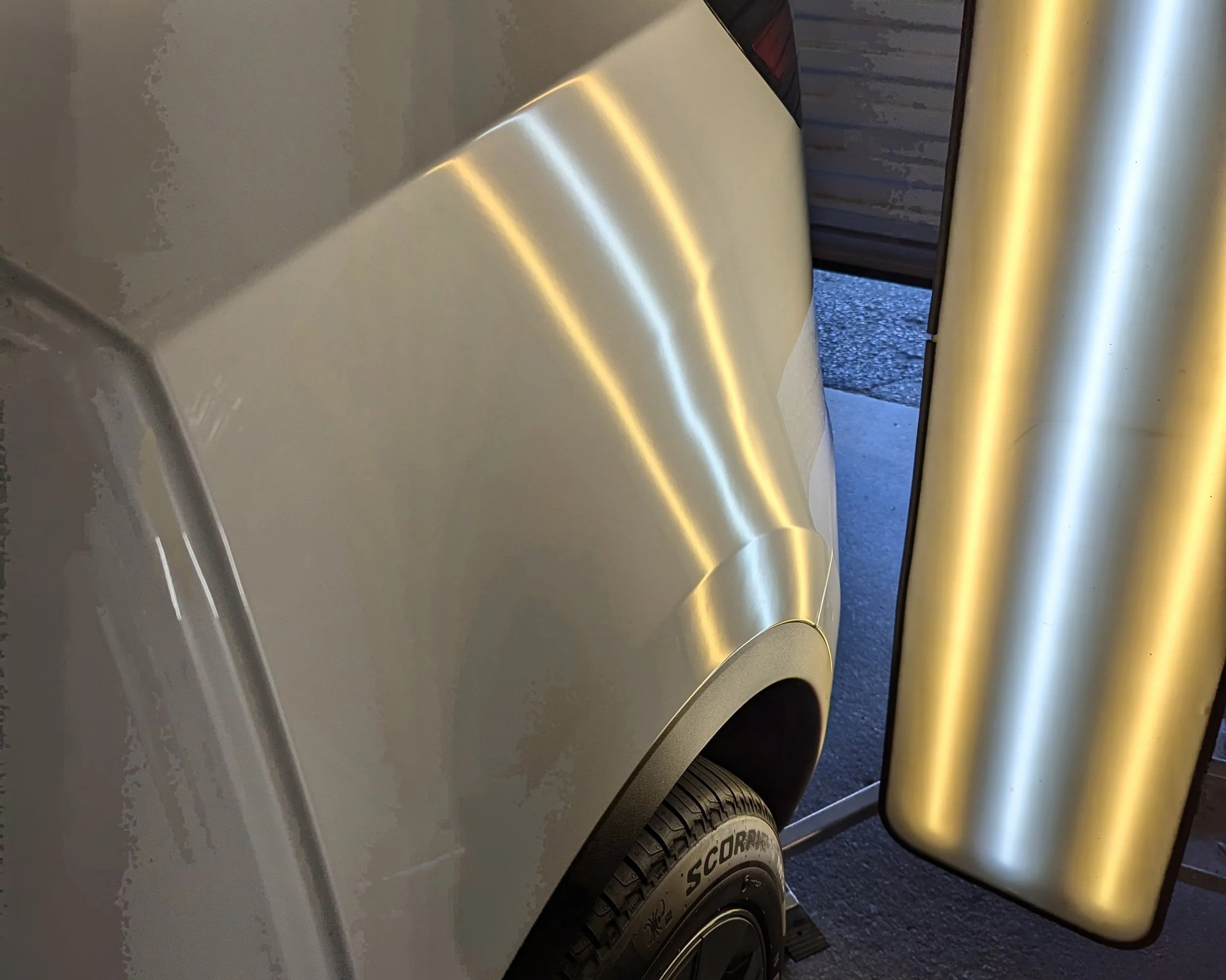 Close-up of a metallic silver garage door opener with a door partially open, revealing a concrete driveway outside.
