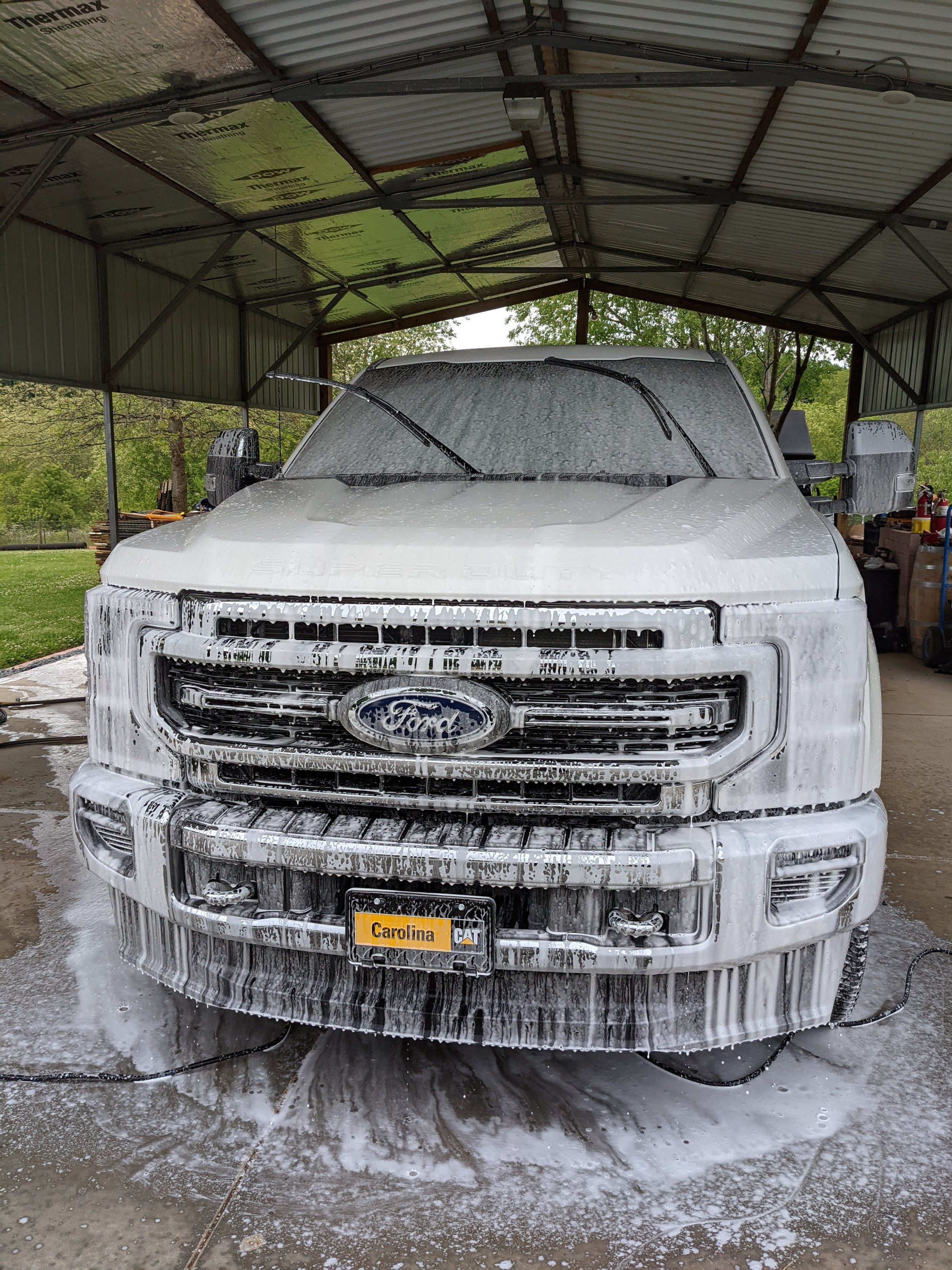 White Ford truck being washed with soap and foam in a metal carport.