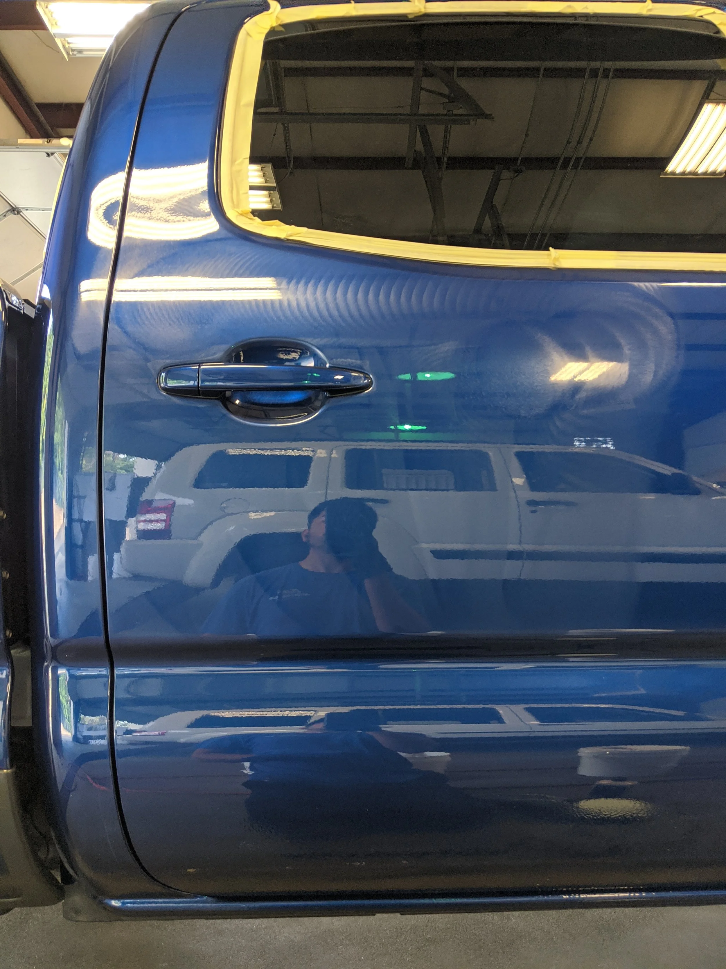 Blue car door with yellow masking tape around the window opening, inside a garage.