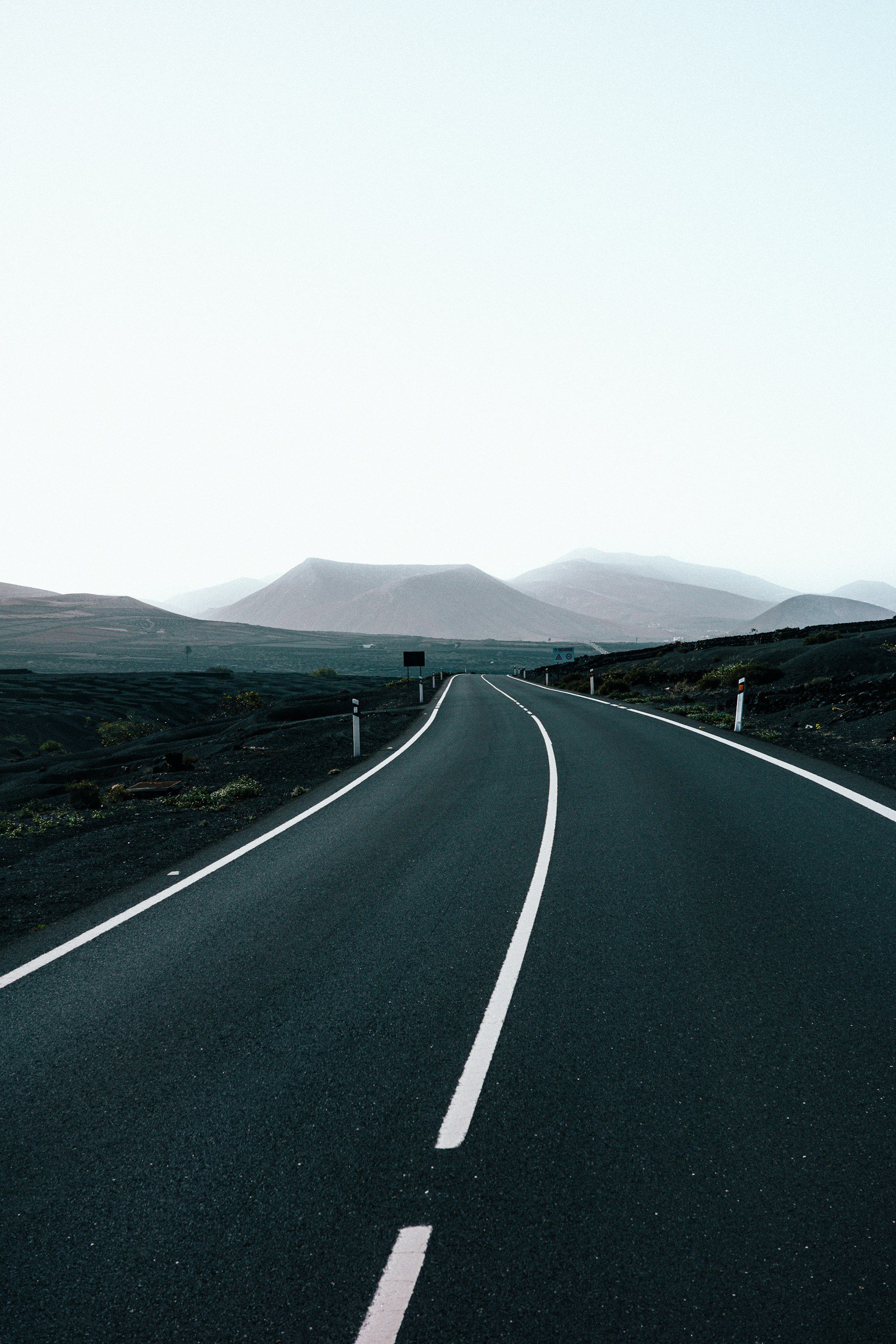 Carretera en un paisaje desértico con montañas borrosas al fondo, cielo despejado.