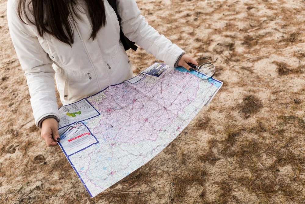 Person holding a map outdoors in a sandy area.