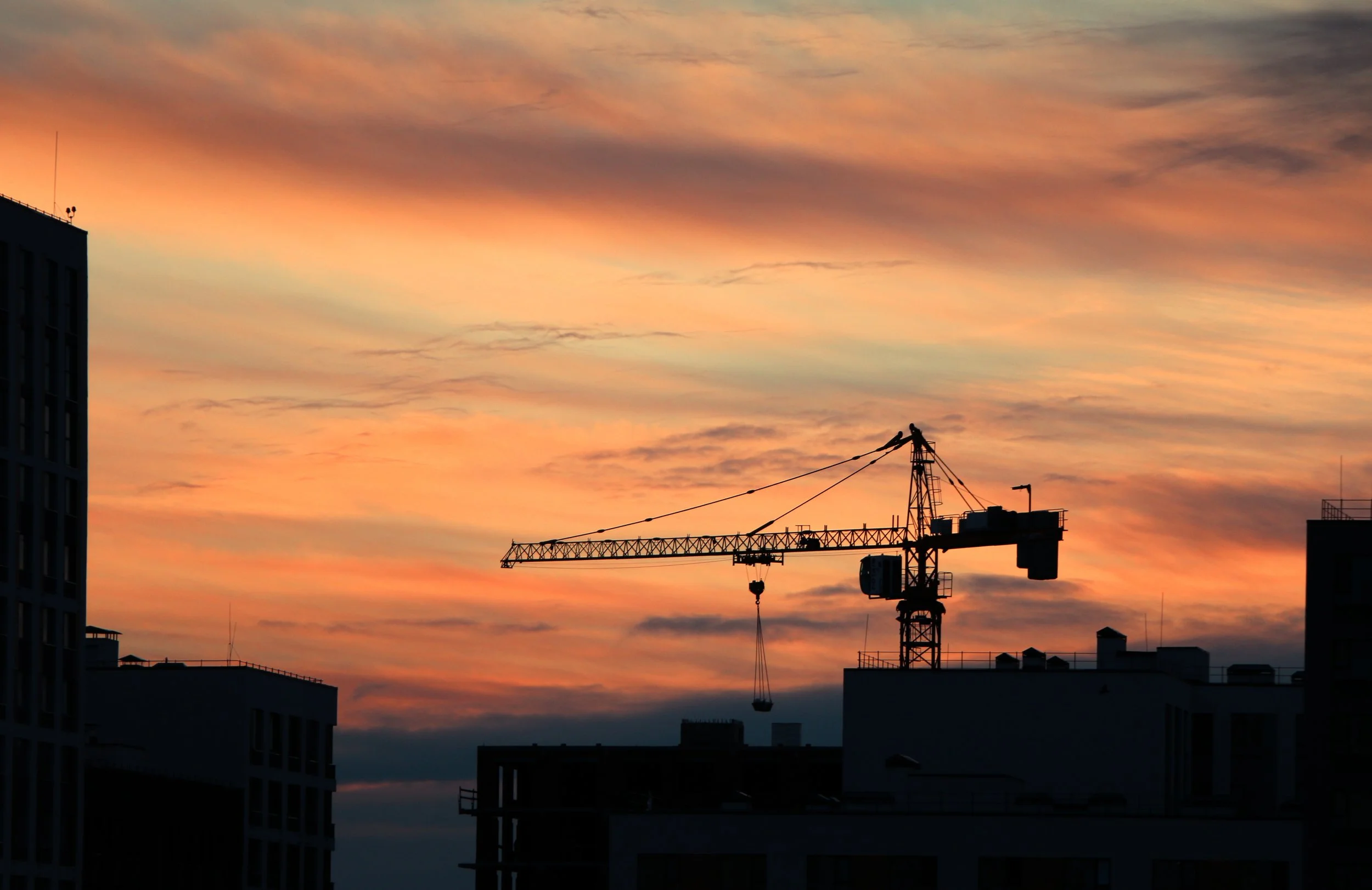 City skyline at sunset with a construction crane in the foreground and clouds in the sky.