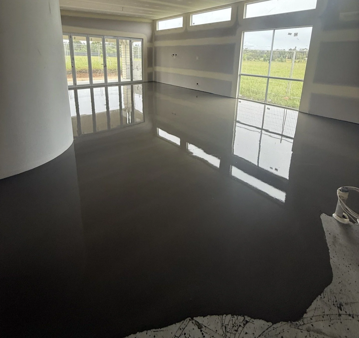 An unfinished room with large windows and a shiny, black epoxy-coated concrete floor.