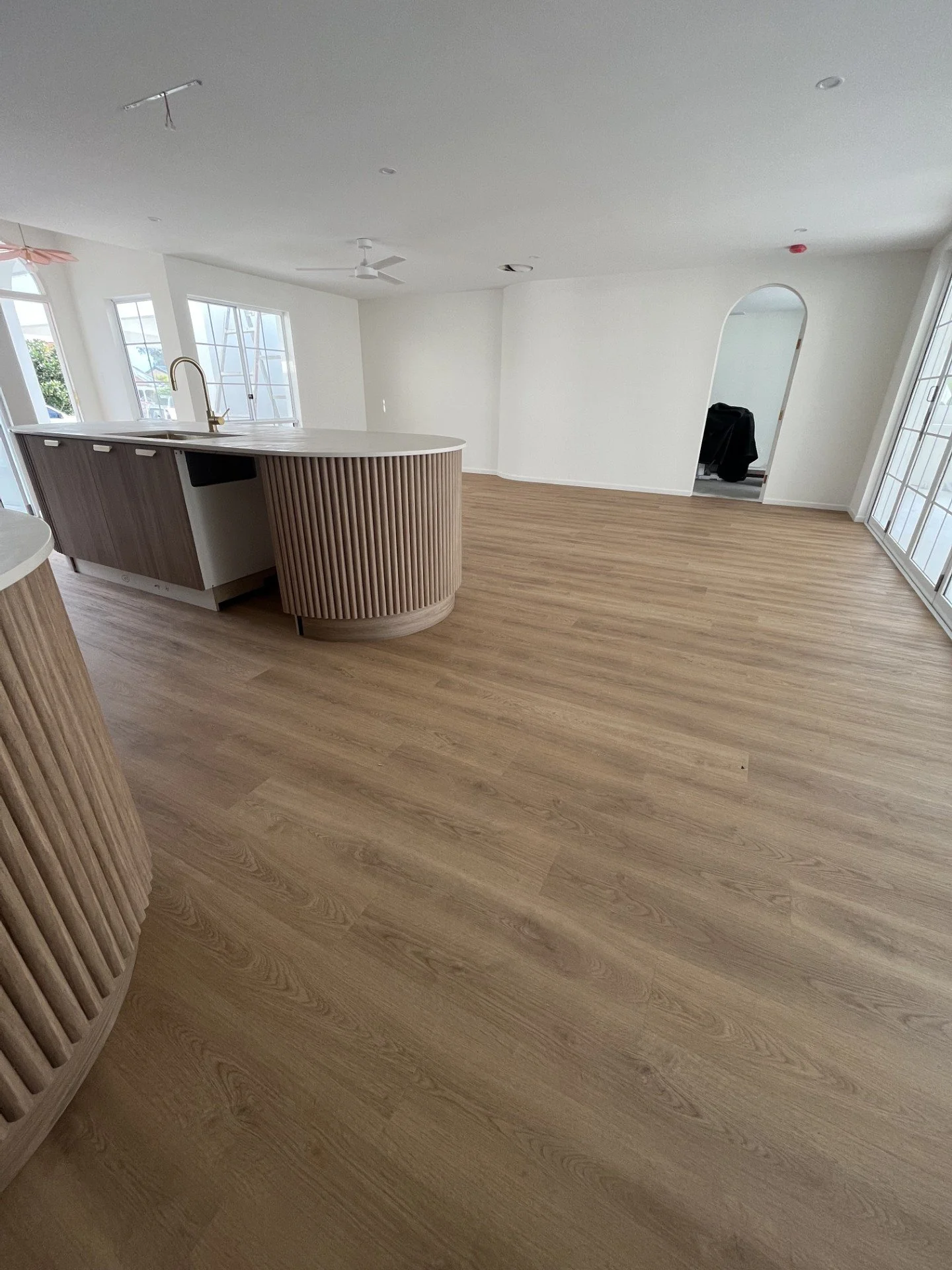 Empty living room with wooden floors, large windows, and a kitchen island.