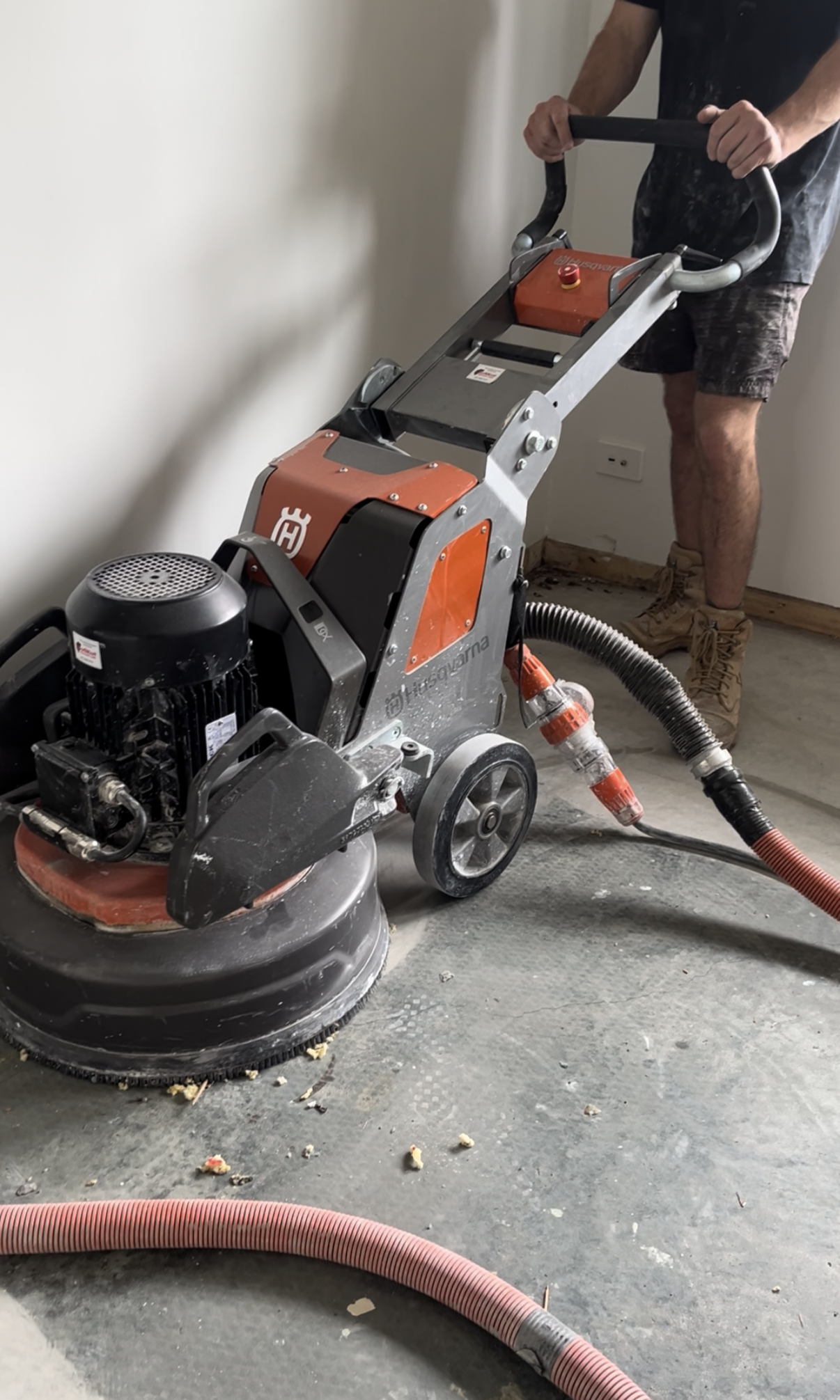A person operating a large, industrial floor grinding machine on a concrete floor during construction or renovation.