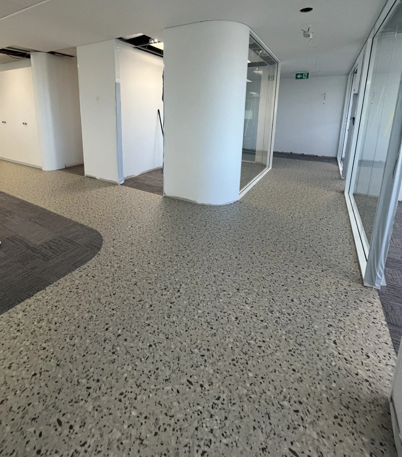 Interior of a building under renovation with white walls, glass partitions, and a terrazzo floor with a patterned section near the bottom left.
