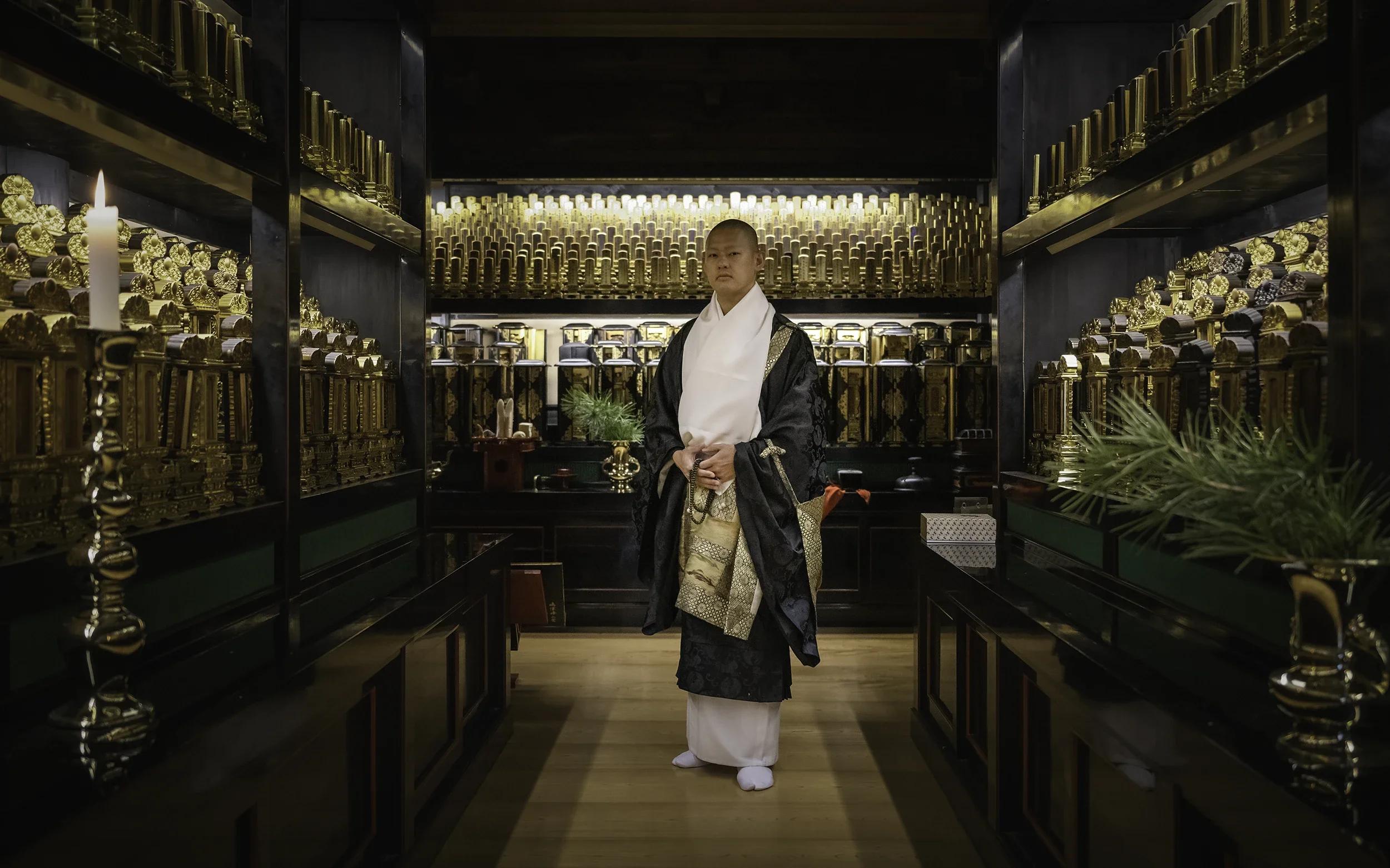 Portrait of a Buddhist monk inside a temple at Mount Koya, Japan, surrounded by traditional Buddhist altars and sacred objects.
