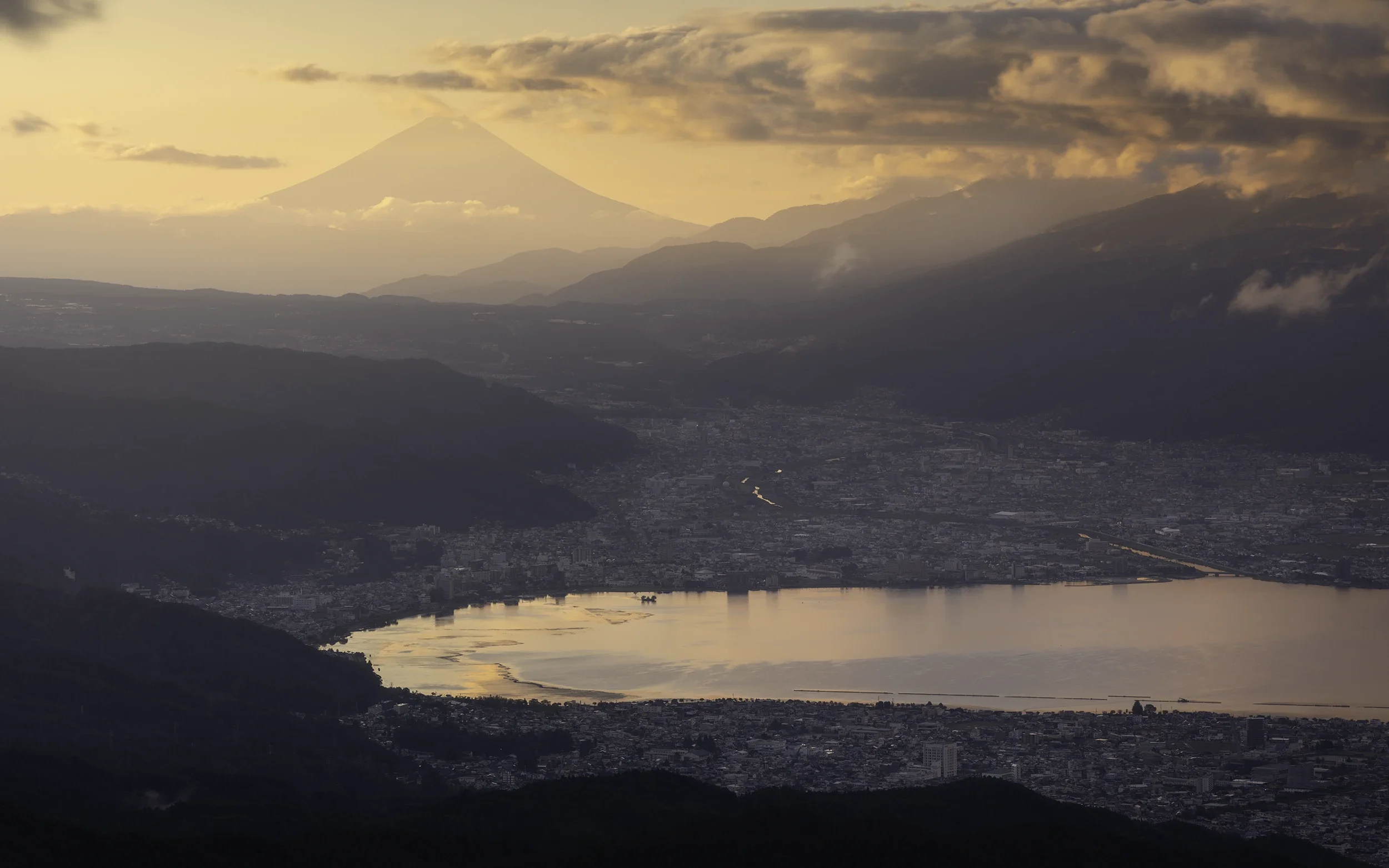 From the highlands overlooking Lake Suwa, Mount Fuji appears layered behind a succession of mountain ranges. As the evening light fades, the landscape gradually dissolves into soft tones and distant silhouettes.