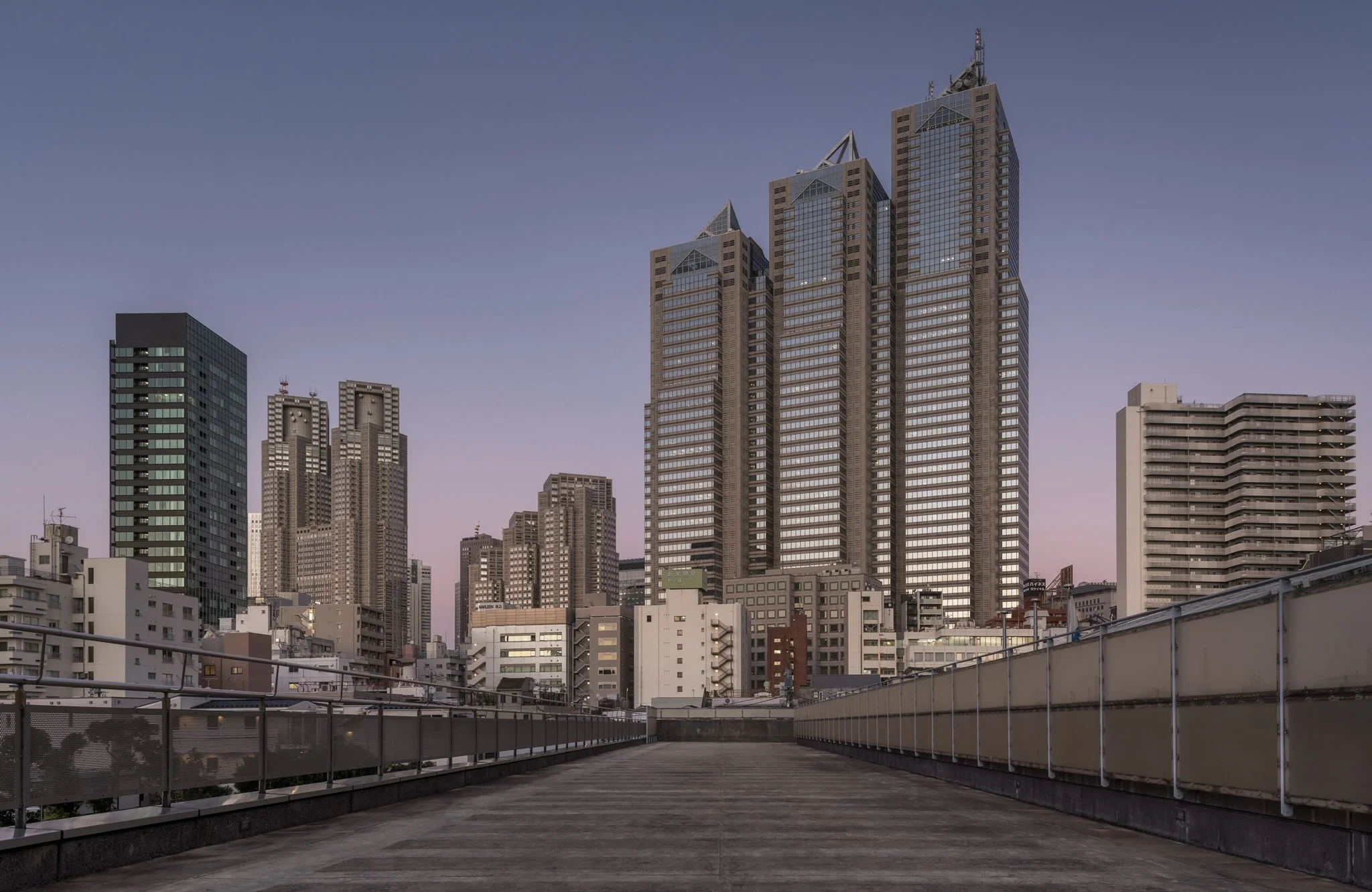 Vue d'une ville avec plusieurs gratte-ciels modernes au crépuscule, vue depuis une terrasse en béton avec une barrière métallique